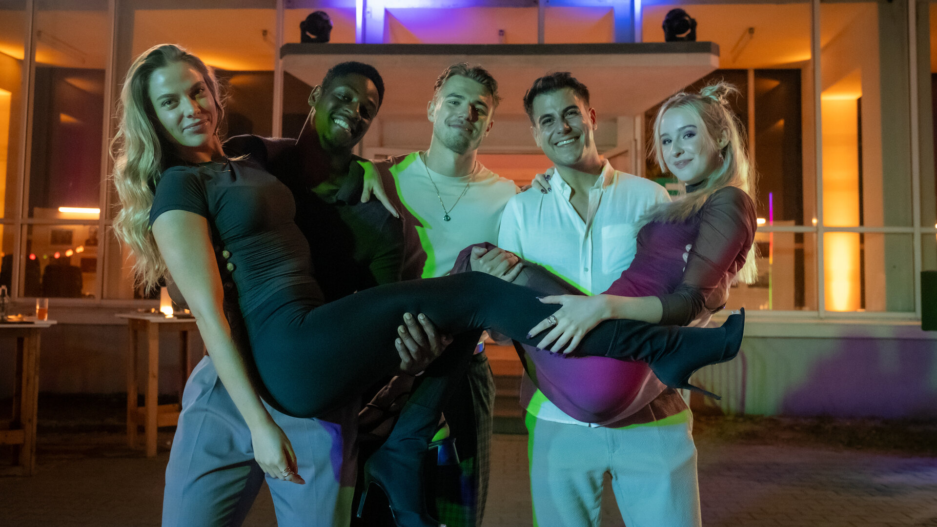 "Blutige Anfänger - Die letzte Ermittlung": Tulani (Ben Andrews Rumler), Phillip (Eric Cordes) und Umut (Uğur Ekeroğlu) stehen nebeneinander vor dem Eingang der PFH. Tulani hält Charlotte (Cheyenne Pahde) auf seinen Armen, Umut Anastasia (Luise Emilie Tschersich). Alle grinsen fröhlich. Es ist dunkel.