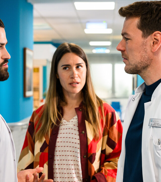 "Bettys Diagnose - Echte Vorurteile": Tarik (Nicolas Fethi Türksever) und Julius (Constantin Lücke) stehen sich im Krankenhausflur gegenüber und schauen sich an. Betty (Henrike Hahn) steht zwischen den beiden und schaut dabei Tarik an.