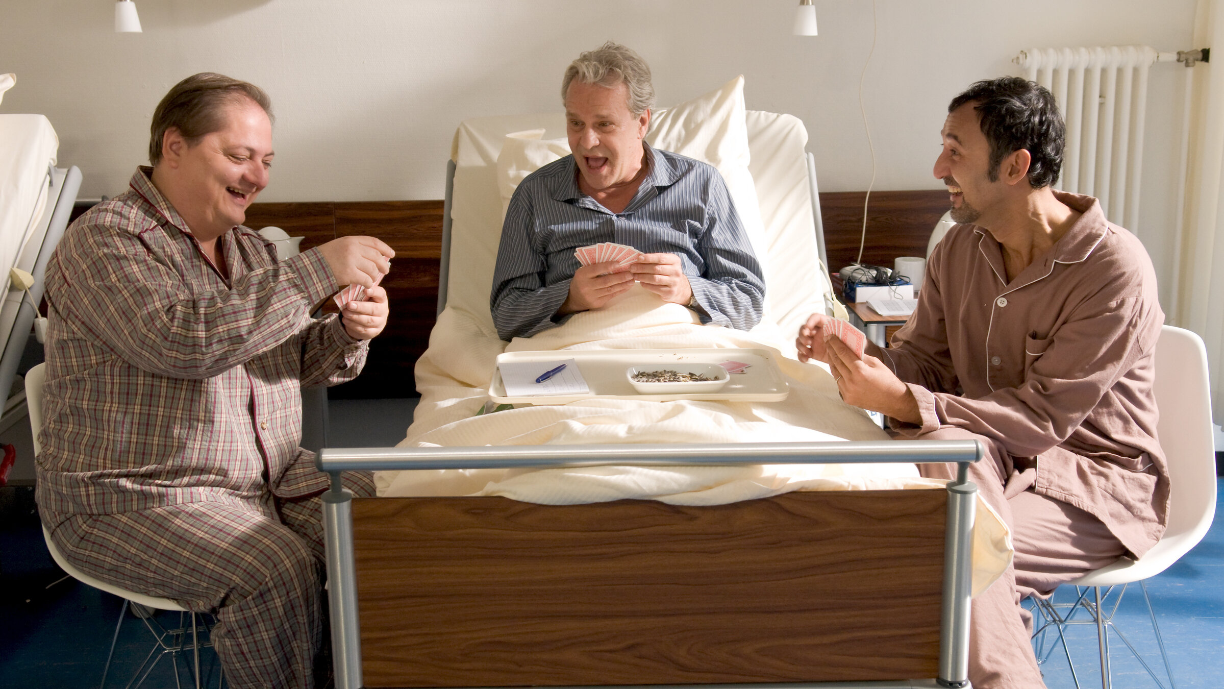 "Heute keine Entlassung": In einem Krankenzimmer sitzt Anton Franzen (Peter Sattmann) in seinem Klinikbett und hält total vergnügt seine Spielkarten in der Hand. Die Zimmergenossen Bernie (Jürgen Tarrach) und Kemal (Ercan Durmaz) sitzen rechts und links neben dem Klinikbett und halten auch Spielkarten in den Händen. Sie vertreiben sich die Zeit mit Kartenspielen.