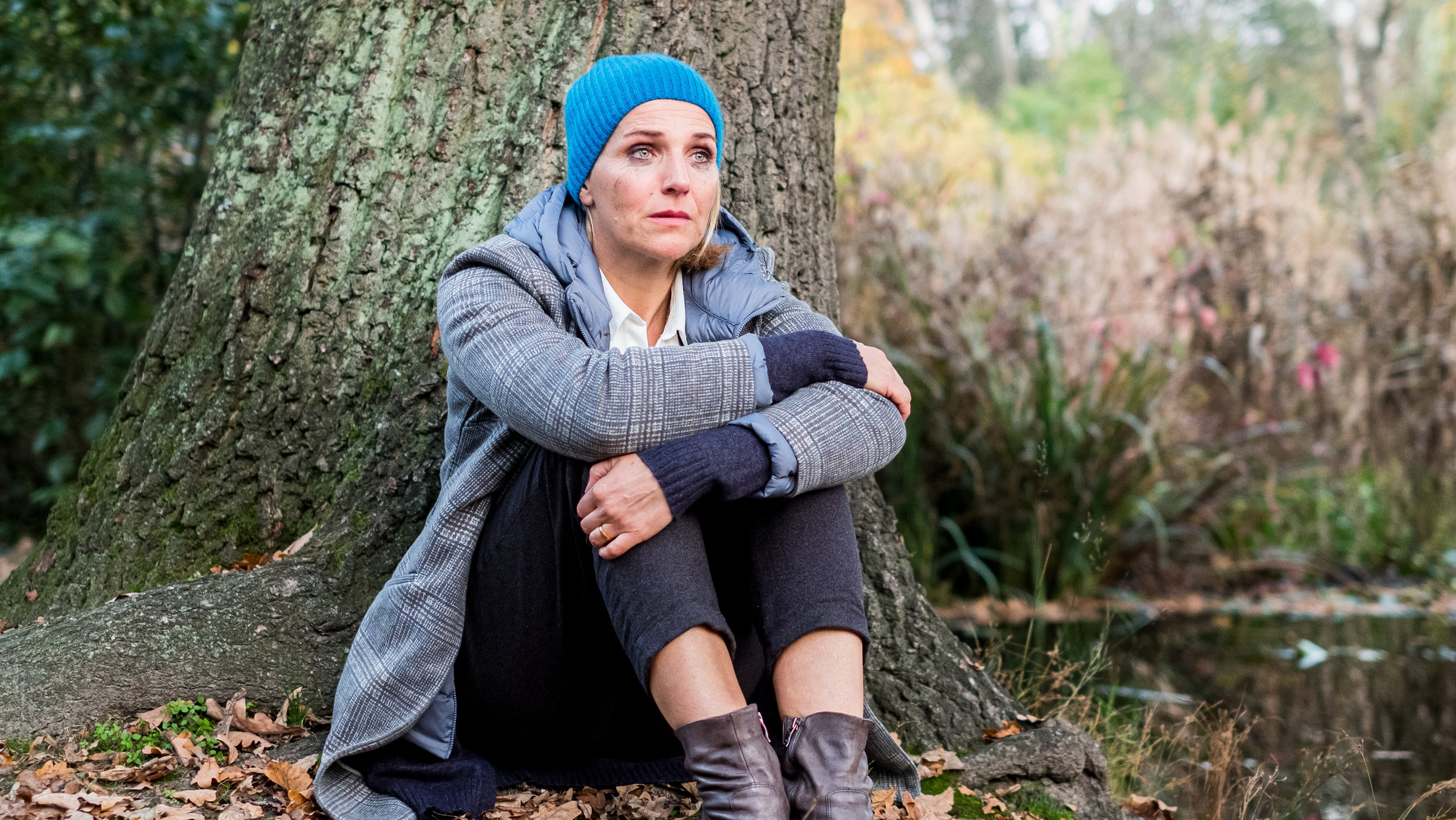 "Fritzie - Der Himmel muss warten - Aus dem Gleichgewicht": Fritzie (Tanja Wedhorn) sitzt auf dem Boden an einen Baum angelehnt. Sie umfasst mit beiden Armen ihre Knie und schaut traurig ins Leere.