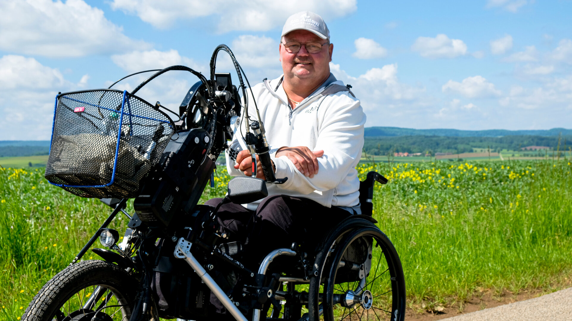 "einfach Mensch - Christian Nachtwey: Von Vielen unterschätzt (3)": Christian Nachtwey sitzt auf dem Handbike an einem Wiesenrand bei Sonnenschein. Er blickt lächelnd in die Kamera.