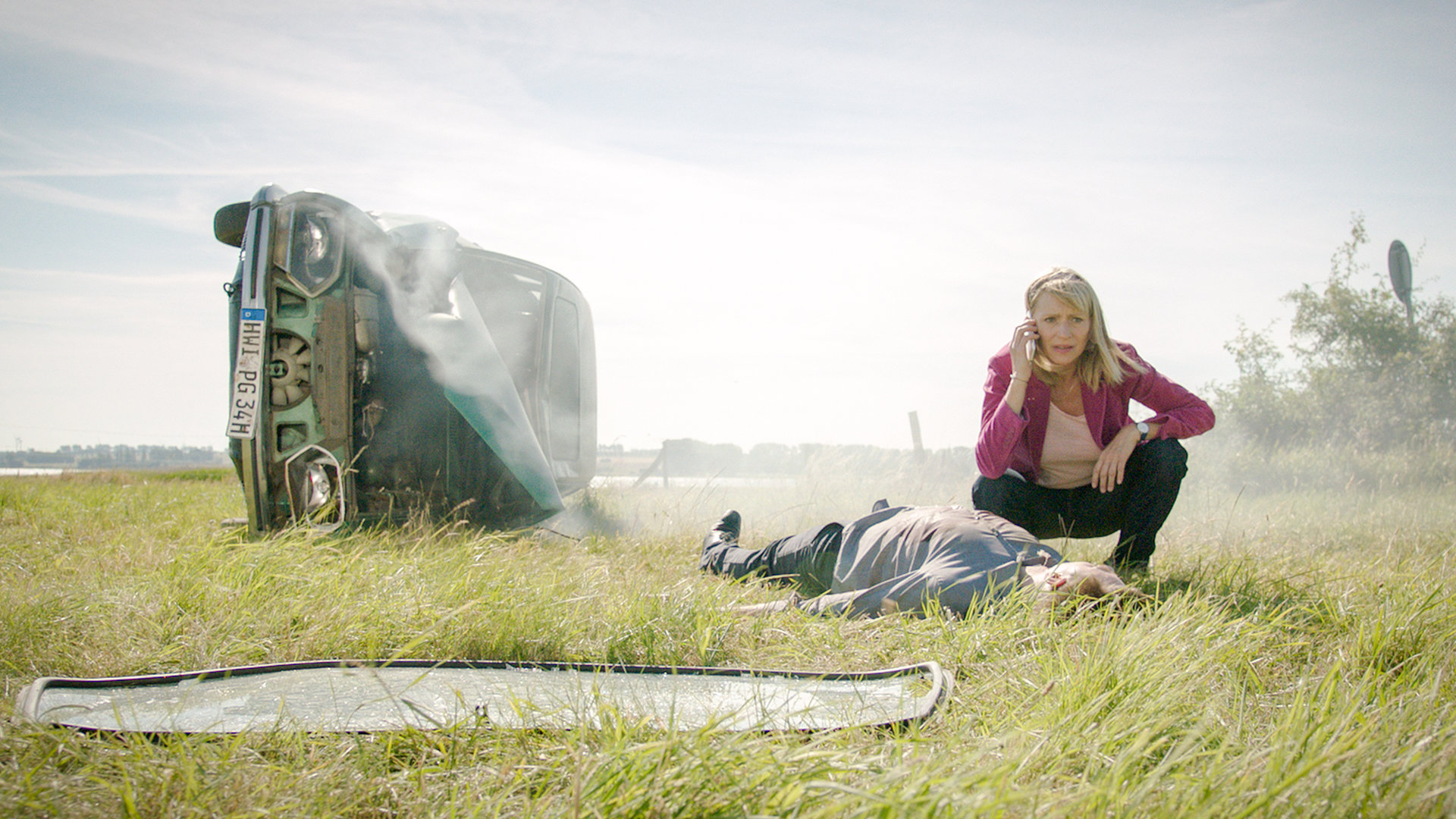 „SOKO Wismar – Aus der Kurve“: Roswitha Prinzler (Silke Matthias) hockt auf einer Wiese und telefoniert. Vor ihr liegt der reglose Jan Lehmann (Christopher Fliether). Etwas daneben liegt ein demolierter Wagen auf die Fahrerseite gekippt, im Hintergrund ist eine Landstraße.
