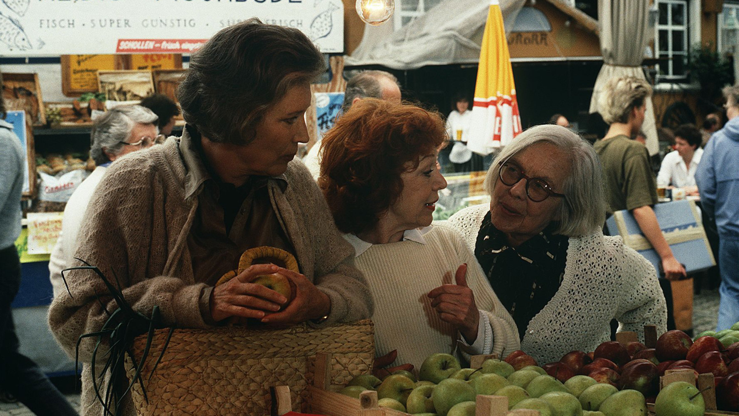 "Der Landarzt - Aus alten Zeiten": Olga Mattiesen (Antje Weisgerber) steht vor einem Obststand neben Gräfin Bea (Gisela Trowe) und Berta (Gerda Gmelin) und schaut beide konzentriert an.
