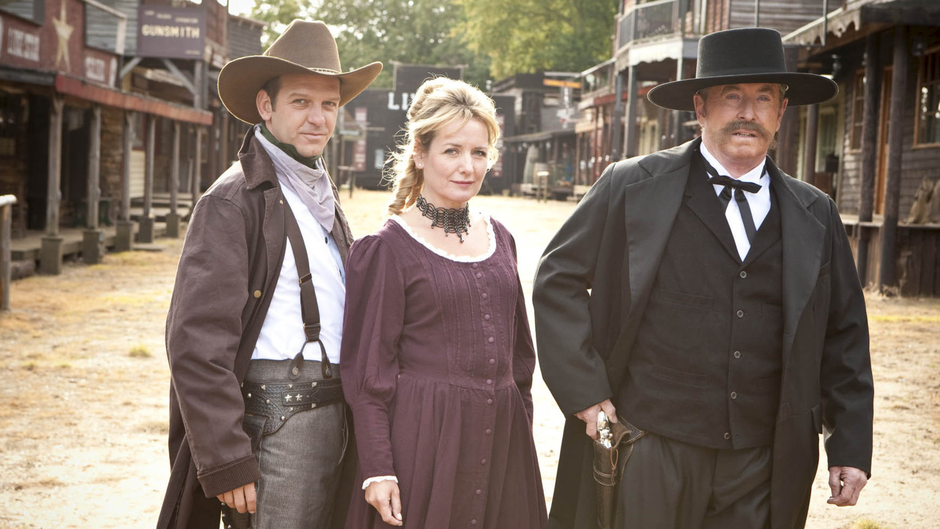 "Inspector Barnaby - Blut am Sattel": DS Ben Jones (Jason Hughes), Susan Fincher (Caroline Langrishe) und DCI Tom Barnaby (John Nettles) stehen in Western-Kostümen nebeneinander.