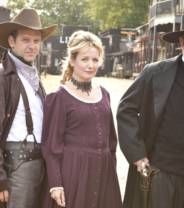 "Inspector Barnaby - Blut am Sattel": DS Ben Jones (Jason Hughes), Susan Fincher (Caroline Langrishe) und DCI Tom Barnaby (John Nettles) stehen in Western-Kostümen nebeneinander.