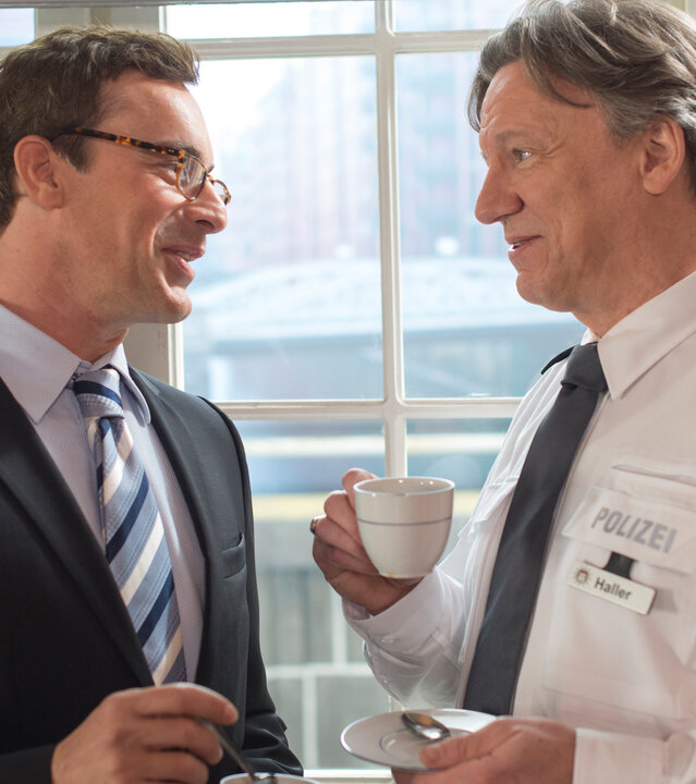 "Notruf Hafenkante - Party-Crasher": Harald Brodersen (Gedeon Burkhard) und Wolf Haller (Hannes Hellmann) stehen sich mit einer Kaffeetasse in der Hand gegenüber und unterhalten sich.