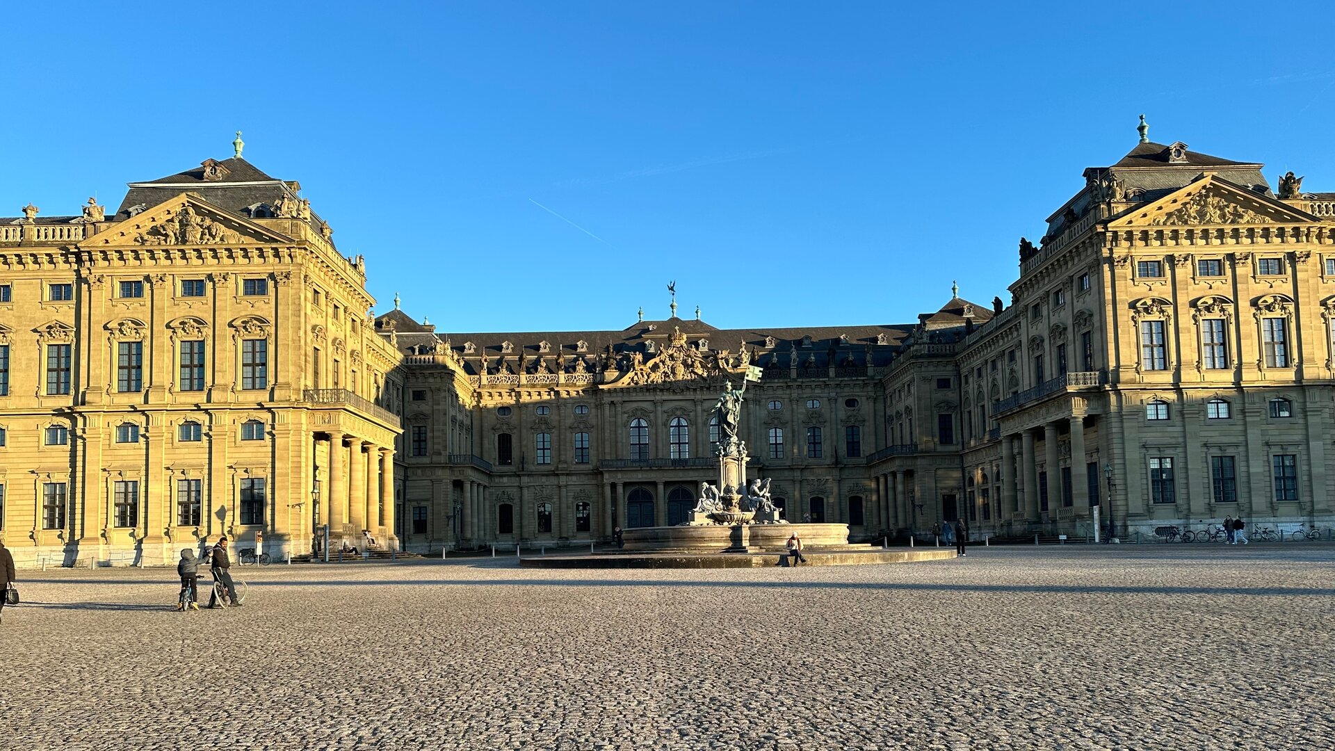"Abschlussgottesdienst zum Katholikentag - Hab Mut, steh auf ...und geh!": Unter blauem Himmel liegt der gepflasterte Residenzplatz, dahinter dahinter liegt die Würzburger Residenz, ein Barockschloss.