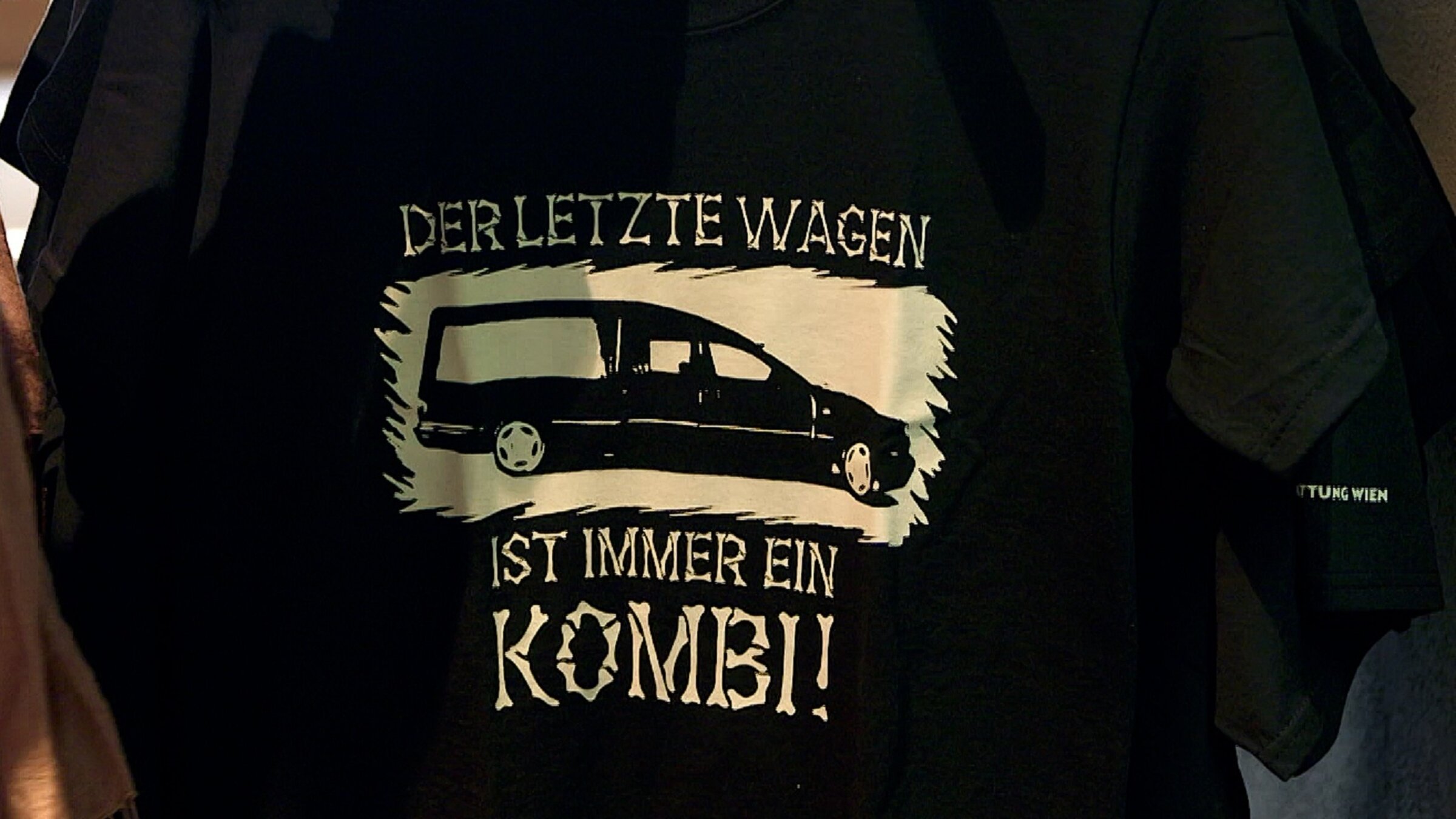 "Tabu Tod (2/2) - Abschied und Trauer": Schwarzes T-Shirt mit einem Leichenwagen und der Aufschrift „Der letzte Wagen ist immer ein Kombi“.