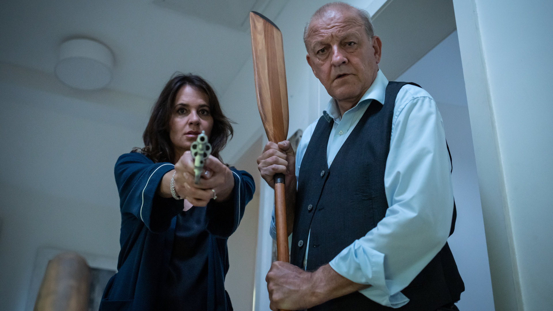 "Wilsberg - Wellenbrecher": Tanja Steinthal (Stephanie Eidt) hält einen Revolver und Georg Wilsberg (Leonard Lansink) ein Ruder in der Hand, um gegen den Einbrecher gerüstet zu sein.