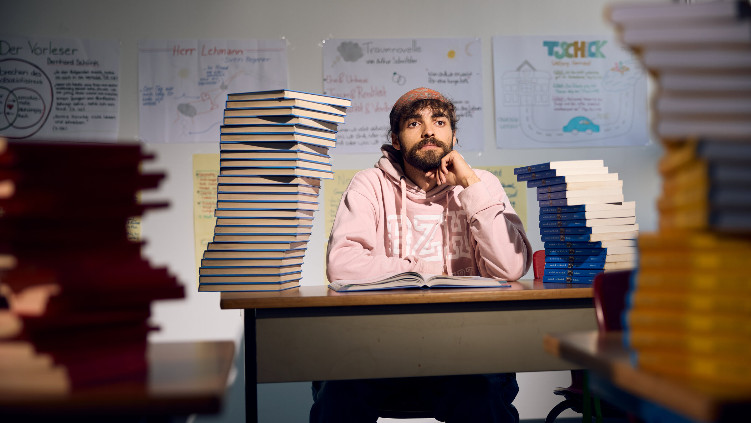 "37°Leben - Lebensretter Schule: Abbruch oder Neuanfang": Marvin sitzt auf einer typischen Schulbank. Vor ihm liegt ein Berg an Schulbüchern. Im Hintergrund hängen Plakate mit Lerninhalten.