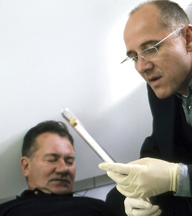 "Der letzte Zeuge - Die sich nach Liebe sehnen": Dr. Robert Kolmaar (Ulrich Mühe) begutachtet die Leiche von Jakob Fänger (Manfred Lehmann) am Tatort. Er schaut sich außerdem einen Gegenstand an.