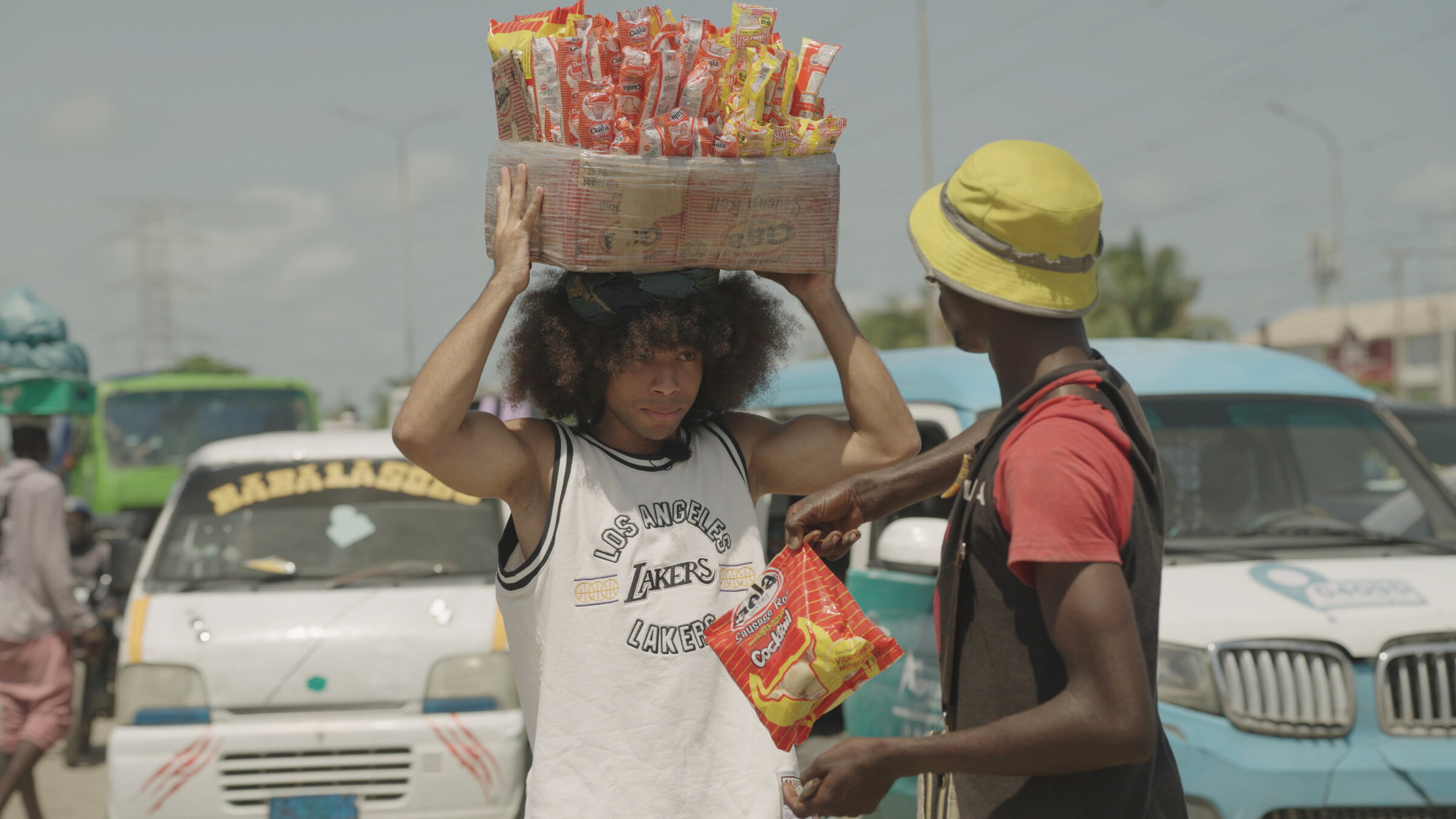 "Hype - die Noelgoescrazy Story": Noel Robinson steht zwischen Autos auf einer Straße in Lagos, Nigeria, auf dem Kopf trägt er einen Korb voller Snacks.