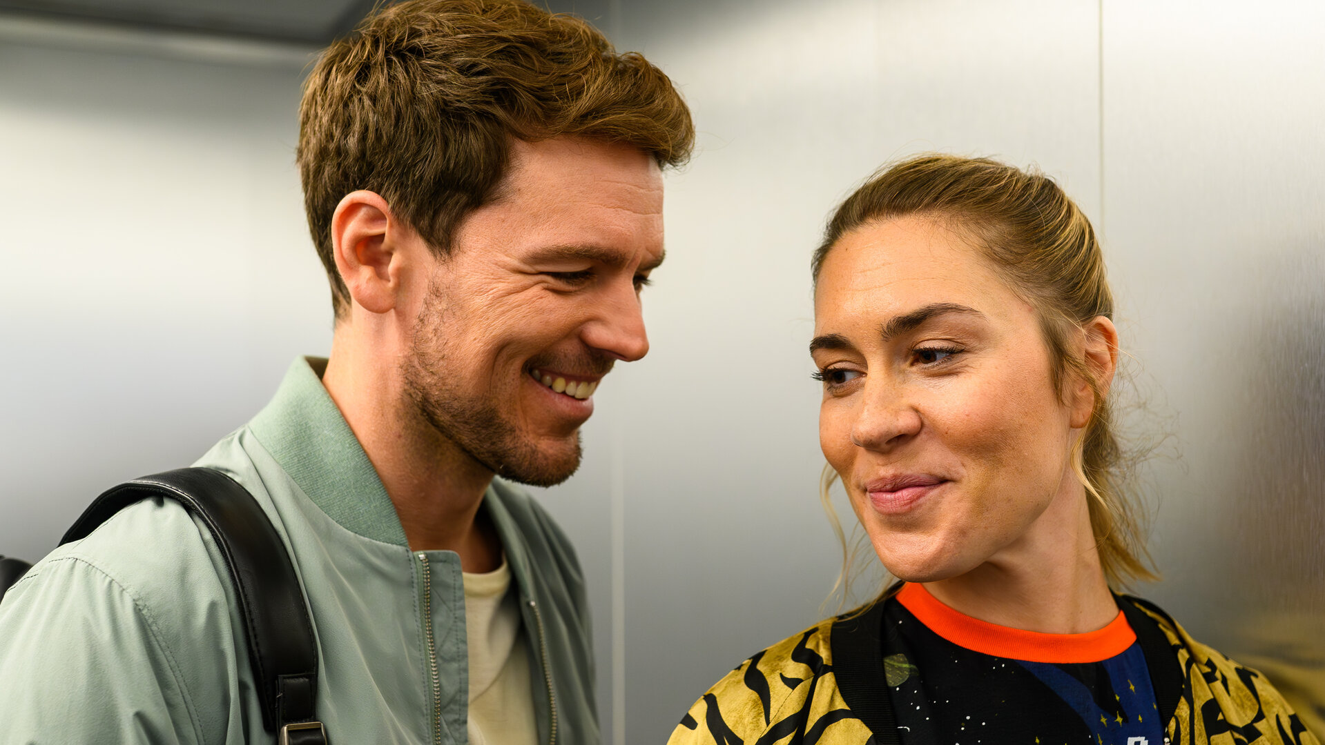 "Bettys Diagnose - Letzte Reise": Dr. Julius Walden (Constantin Lücke) und Betty Hertz (Henrike Hahn) stehen im Aufzug und unterhalten sich lächelnd.