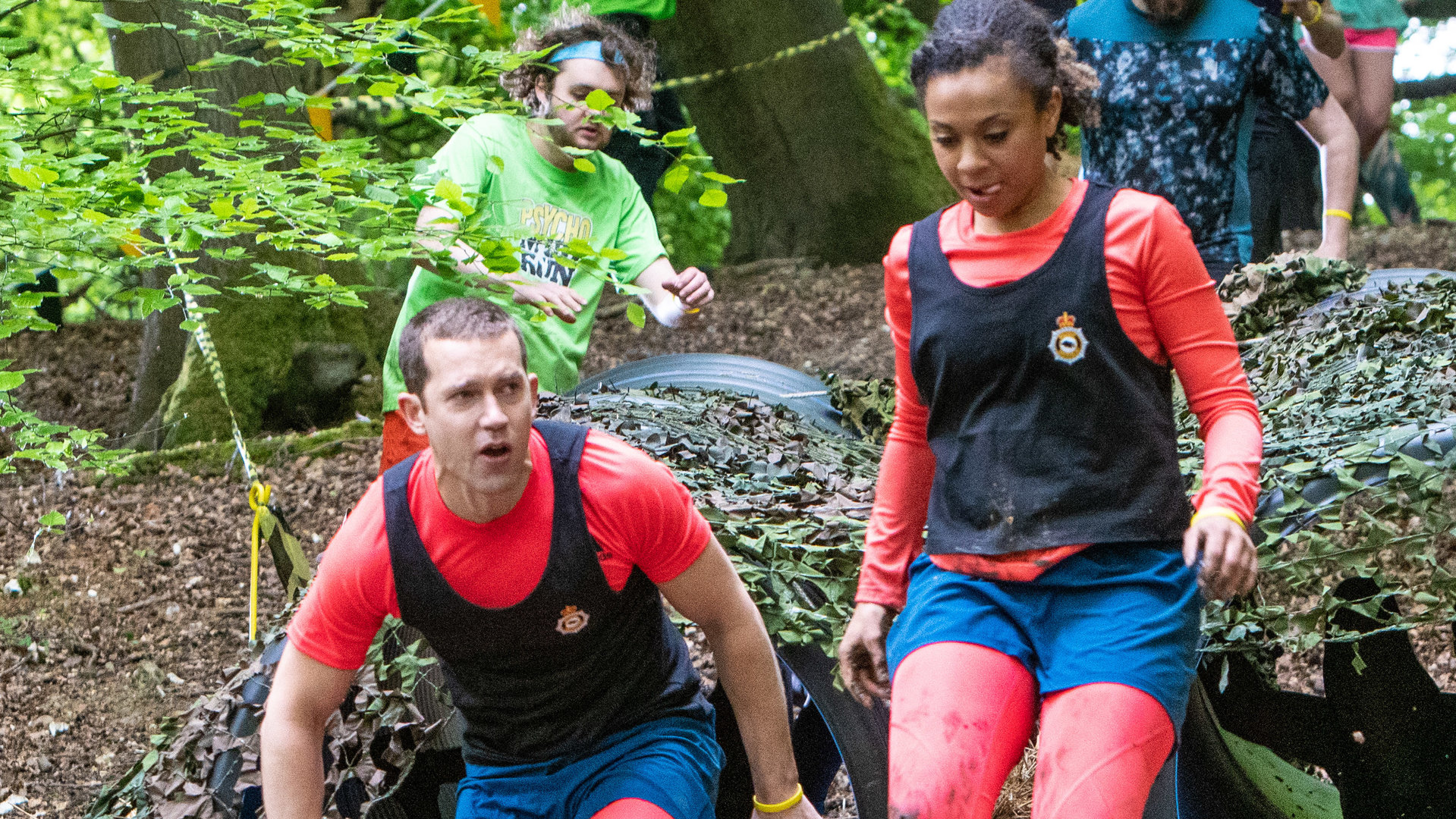 "Inspector Barnaby - Leichzeit am See": Detective Sergeant Jamie Winter (Nick Hendrix) und Police Constable Jade-Marie Pierce (Eleanor Fanyinka) beim Mud Run. Sie kommen gerade aus zwei nebeneinander liegenden Rohren, vor ihnen liegen zahlreiche Autoreifen, über die sie springen müssen.