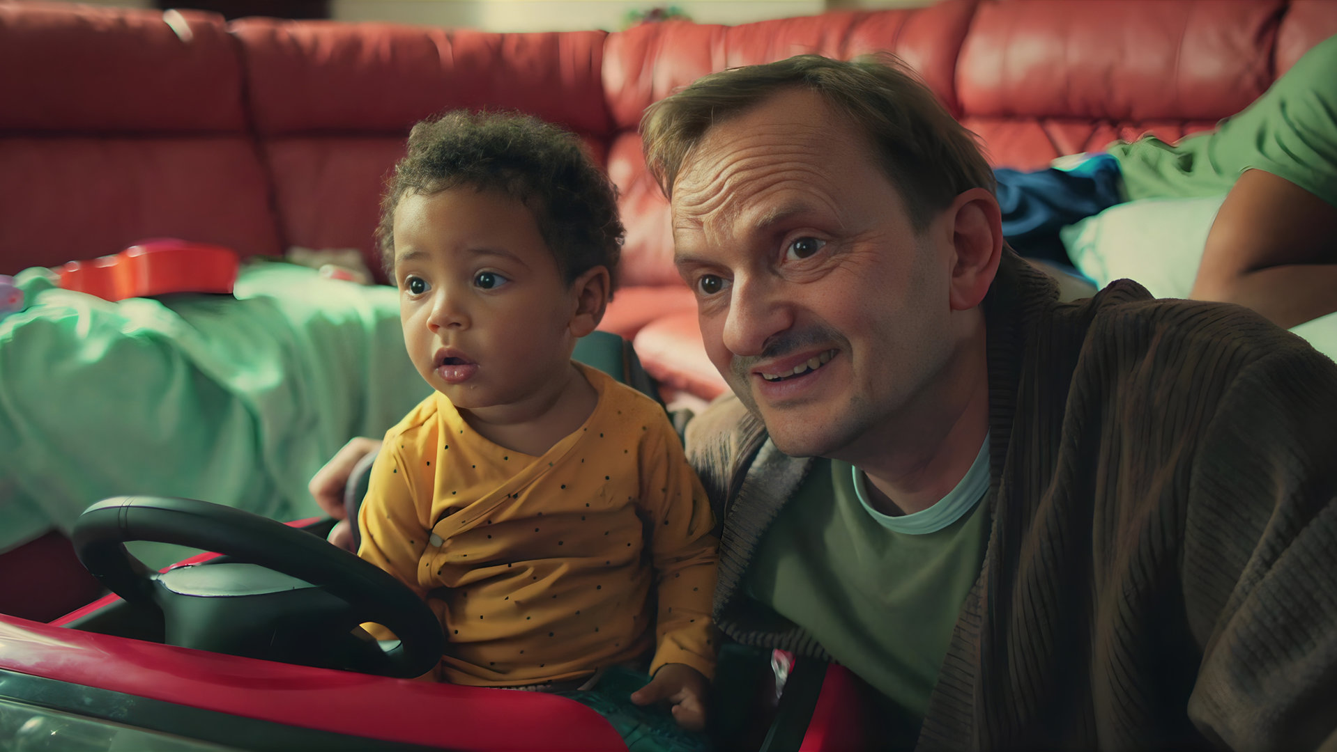 "Doppelhaushälfte - Frida": Baby Frida (Rio Disselhoff) sitzt in einem Spielzeugauto. Andi (Milan Peschel) sitzt neben ihr und hat seinen Arm um sie gelegt.