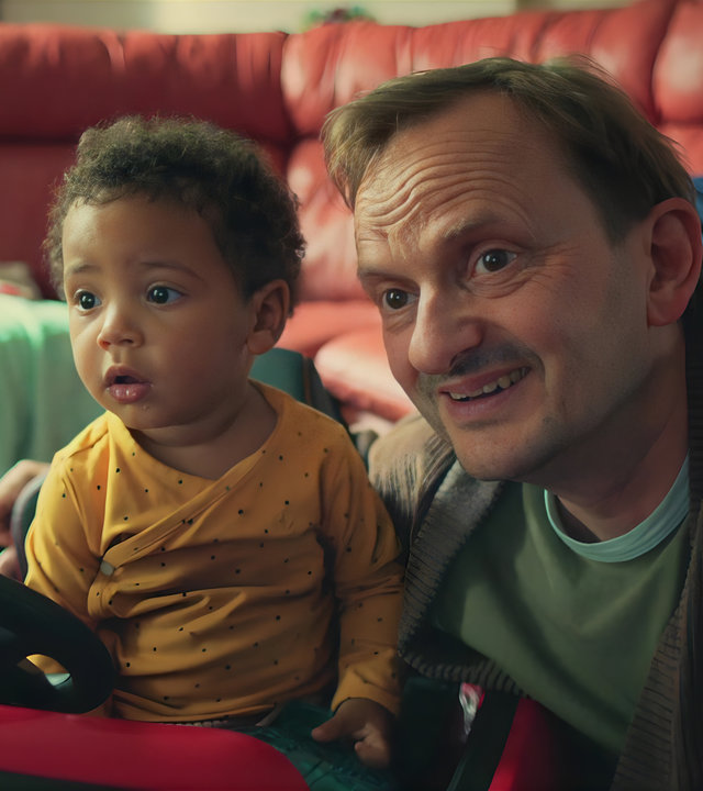 "Doppelhaushälfte - Frida": Baby Frida (Rio Disselhoff) sitzt in einem Spielzeugauto. Andi (Milan Peschel) sitzt neben ihr und hat seinen Arm um sie gelegt.