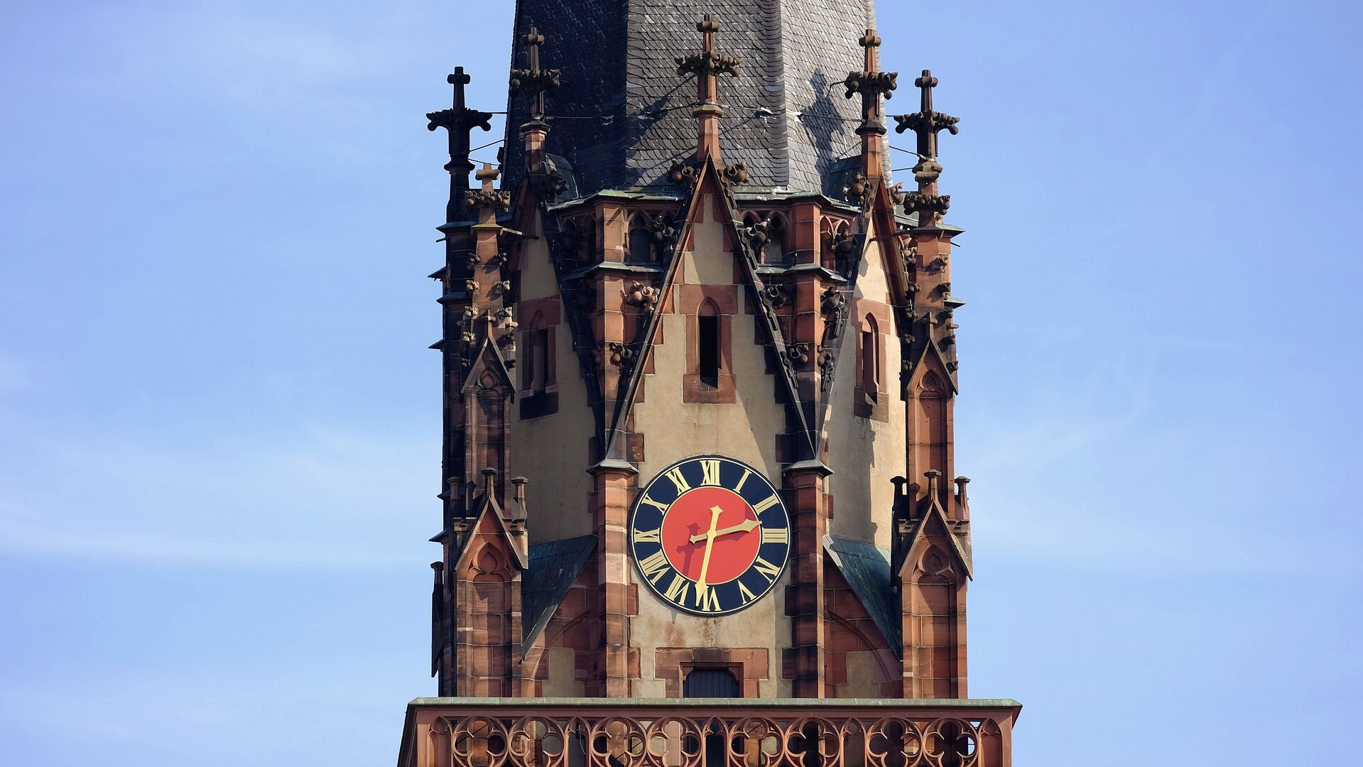 "Evangelischer Gottesdienst - Und Sara lachte": Auf dem Bild ist ein Teil des Turms der Dreikönigskirche in Frankfurt am Main zu seh. Filigrane, aus Stein gemeißelte Kreuze umrunden den Turm im neugotischen Stil, in seiner Mitte befindet sich die rote-blaue Kirchturmuhr mit goldenen Zeigern.