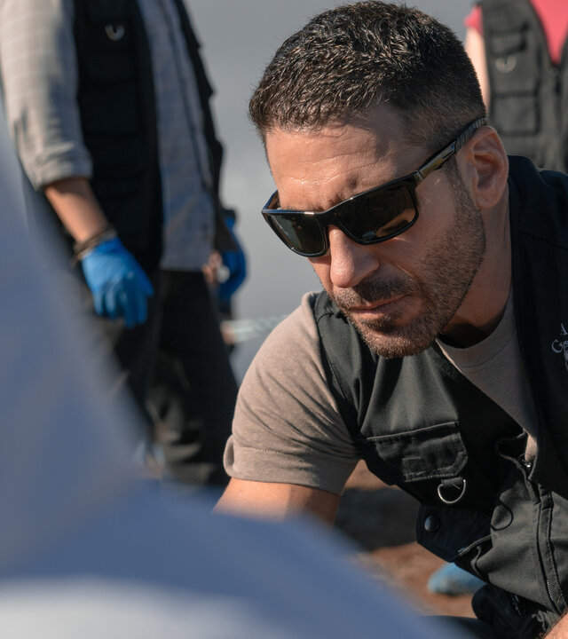 "Weiss & Morales: Eine Frage des Vertrauens": Raúl Morales (Miguel Ángel Silvestre) schaut nach unten. Im Anschnitt befindet sich eine Person mit weißem Schutzanzug vor ihm.