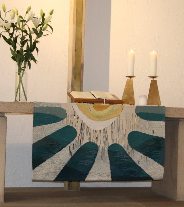 "Evangelischer Gottesdienst: Zeit zum Durchatmen!": Eine aufgeschlagene Bibel liegt auf dem schlichten Altar der Evangelisch-methodistischen Hoffnungskirche in Stuttgart zu sehen. Auf dem Altar ist ein blauweißes Tuch ausgebreitet, zwei Kerzenständer mit weißen Kerzen befinden sich rechts, eine Blumenvase mit weißen Blumen steht links auf dem Altar.