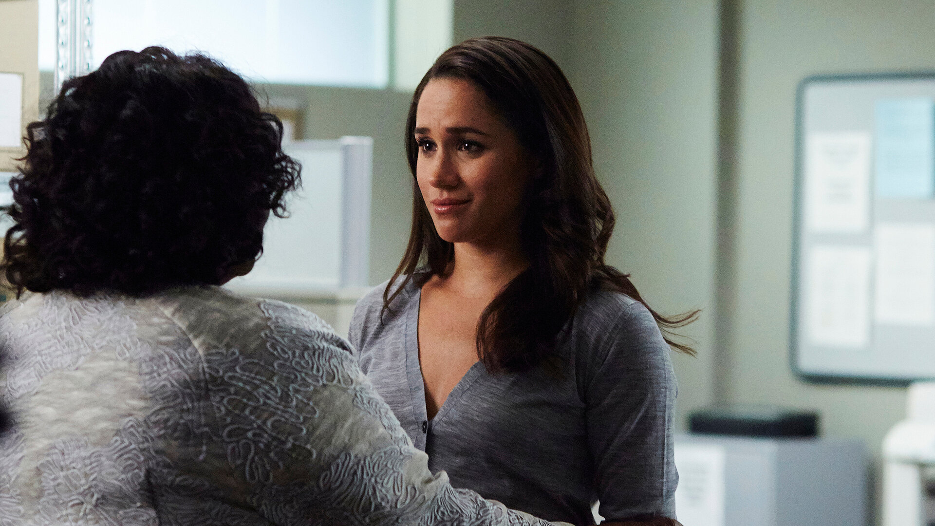 "Suits - Sie ist weg": Rachel (Meghan Markle) steht mit bedrückter Miene vor einer Frau, deren Rücken der Kamera zugewandt ist. Tröstend liegen deren Hände auf Rachels Armen und Rachel scheint für die trostspenden Worte sehr empfänglich.