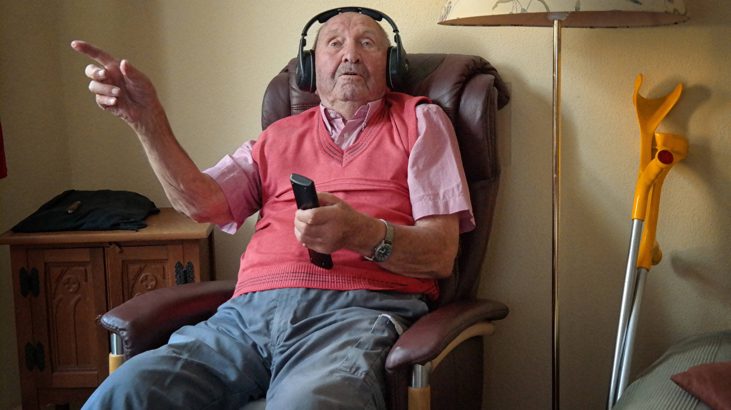 "37° - Mit 100 ist noch nicht Schluss: Alt aber nicht von gestern": Herr Körber sitzt im Sessel und hat Kopfhörer auf. In seiner rechten Hand hält er die Fernbedienung für das Fernsehgerät.