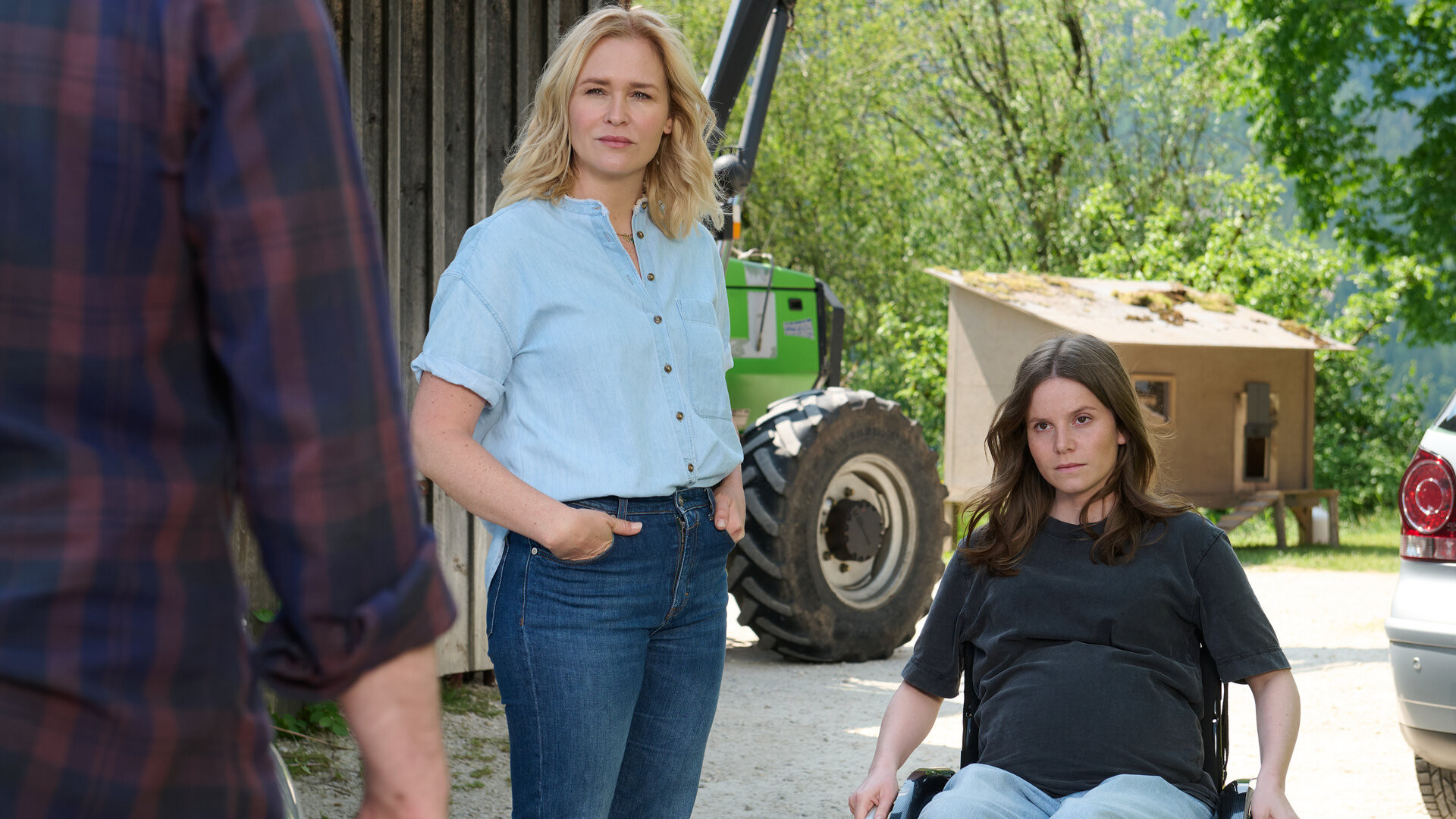 "Lena Lorenz - Harter Bruch": Vor einer Scheune stehen sich Josi Brenner (Muriel Bielenberg) und Paul Zöller (Ron Helbig), der mit dem Rücken zur Kamera steht, gegenüber. Lena Lorenz (Judith Hoersch) steht zwischen ihnen. Die beiden Frauen blicken ernst zu Paul hinüber. Im Hintergrund steht ein Traktor neben einem Hühnerhaus.