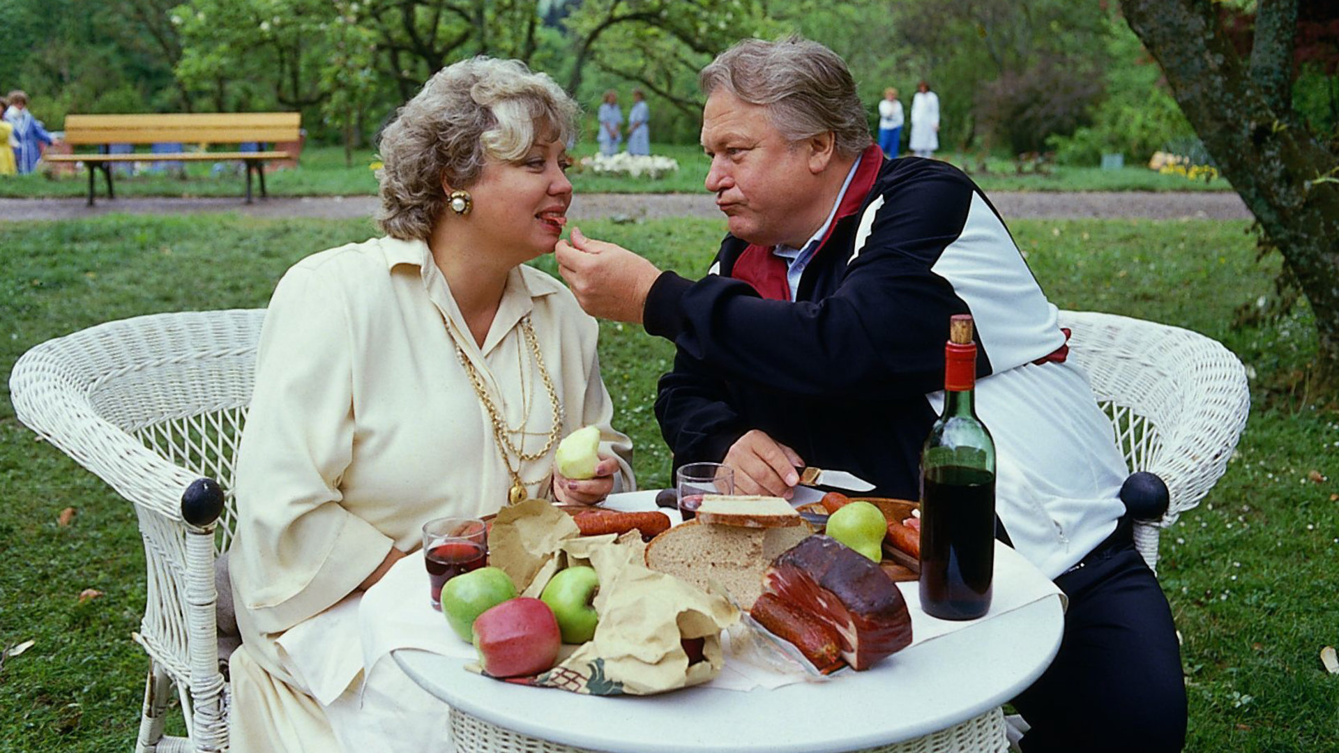"Die Schwarzwaldklinik - Gewichtsprobleme": Frau Kulmbach (Ilse Page) und Herr Kulmbach (Günter Strack) sitzen an einem reich bedeckten Tisch im Park und essen.