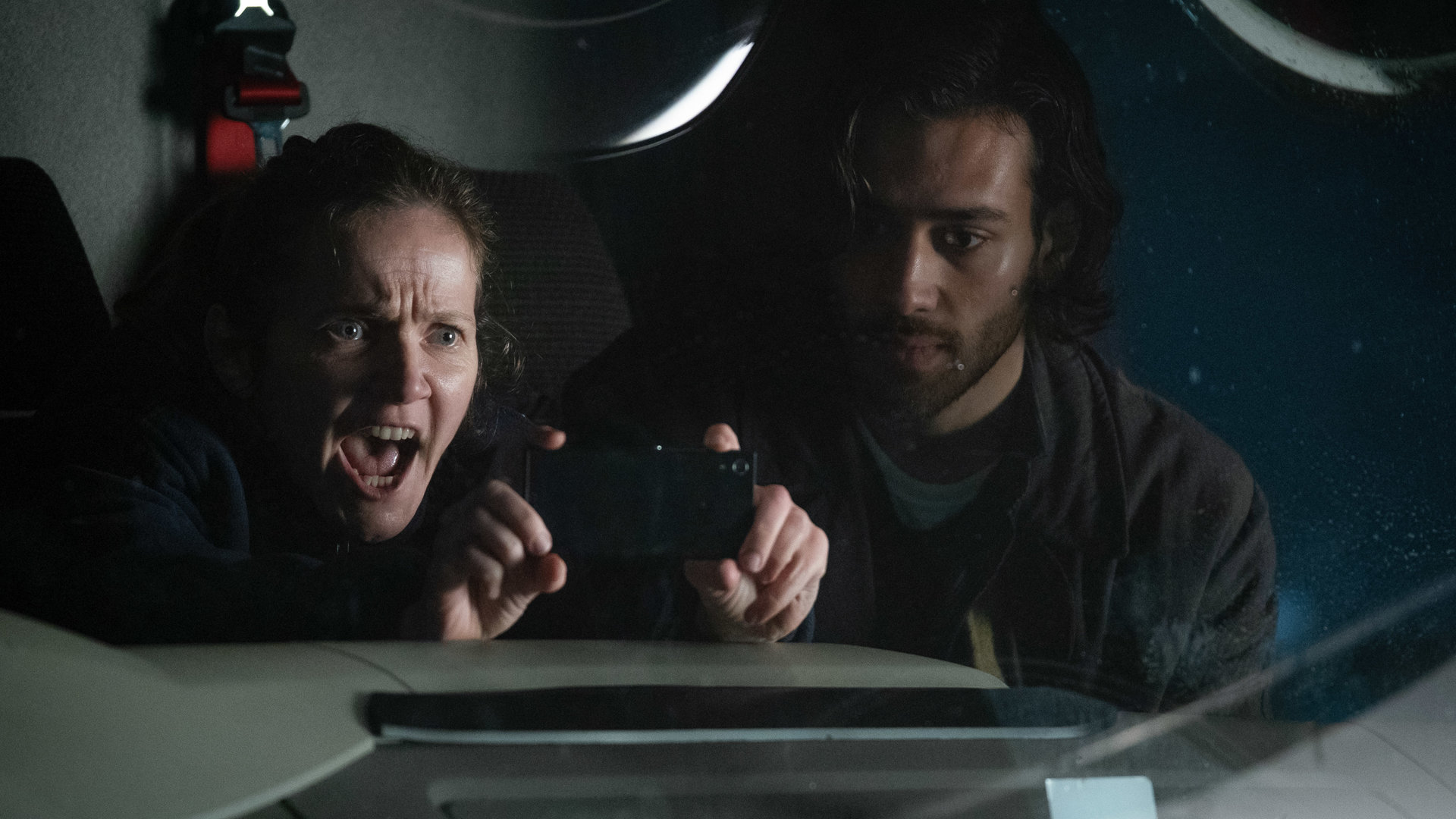 "Years and Years": Edith Lyons (Jessica Hynes) schreit, streckt dabei ihre Hände nach vorne und macht ein Foto. Neben ihr sitzt Viktor Goraya (Maxim Baldry) im Auto.