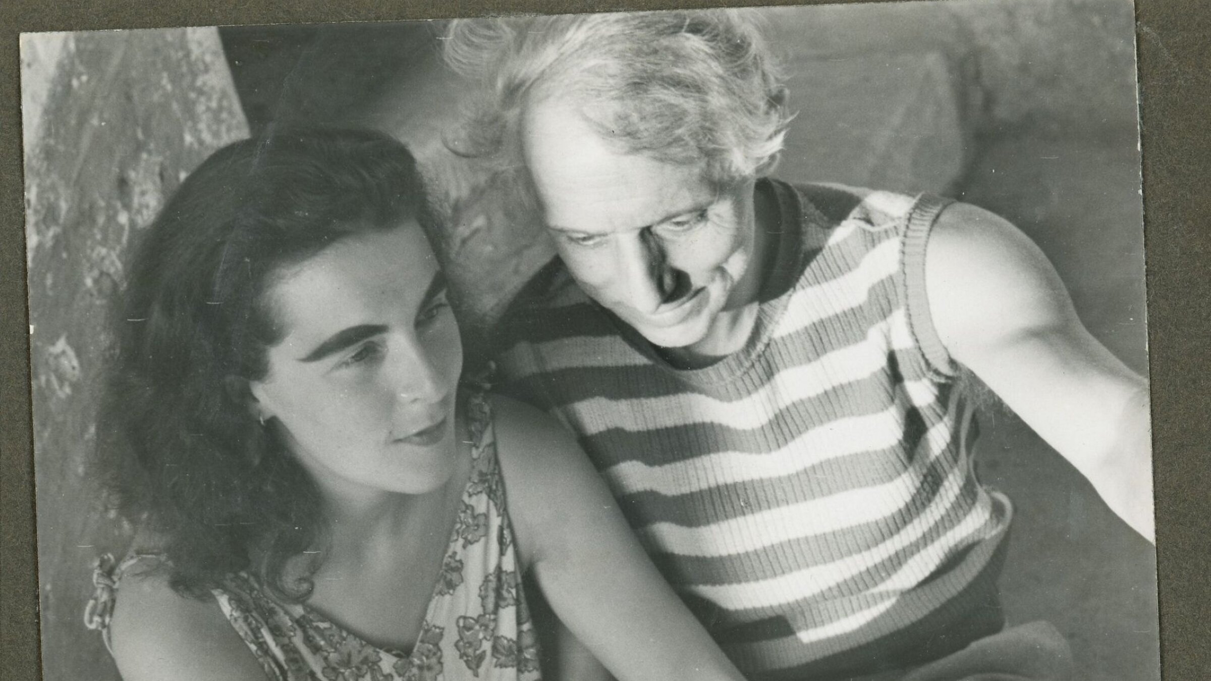 "Max Ernst – Der Surrealist und das Trampeltier": Die Malerin Leonora Carrington und der Maler Max Ernst sitzen nebeneinander an einer Steinwand. Beide lächeln (s/w).