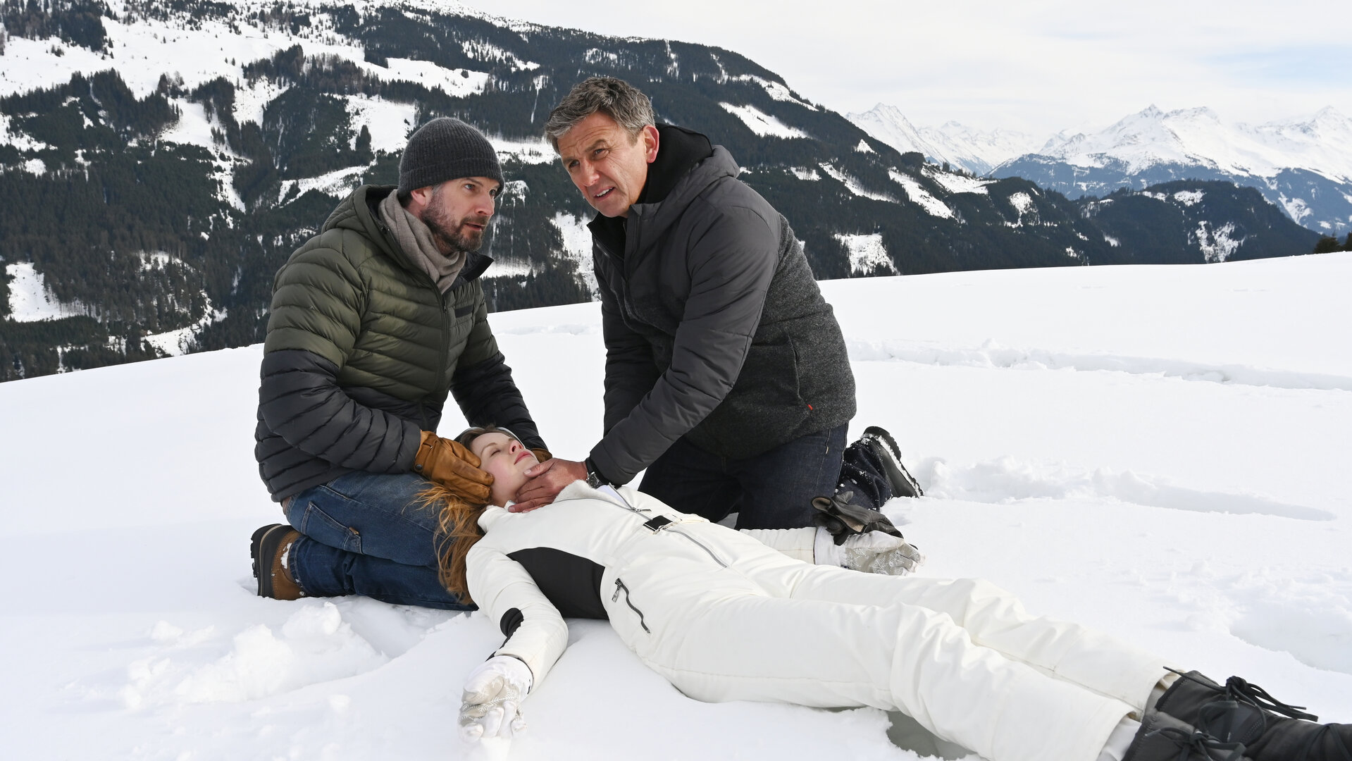 "Der Bergdoktor: Die dunkle Seite des Lichts (2)": Natalie (Emilie Bernsdorf) liegt bewusstlos im Schnee. Ihr Vater Hannes (Simon Böer) und Dr. Martin Gruber (Hans Sigl) knien neben ihr und schauen besorgt.