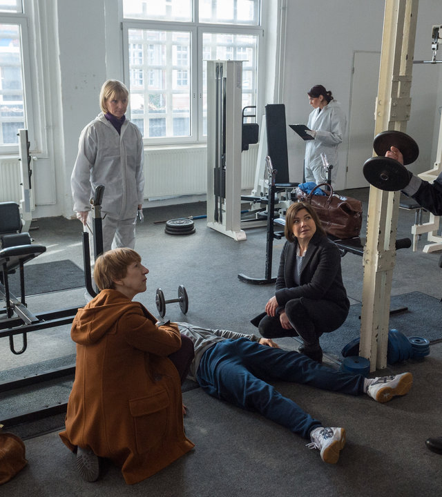 "SOKO Wismar – Knock-out": Zwischen Fitnessgeräten liegt die Leiche von Ronny Schnell (Mark Filatov). Daneben hocken Helene Sturbeck (Katharina Blaschke) und Katrin Börensen (Claudia Schmutzler). Sie schauen auf Timmermann (Mathias Junge), der eine Hantel hochhält. Im Hintergrund sind Roswitha Prinzler (Silke Matthias) und die KTU bei der Arbeit.