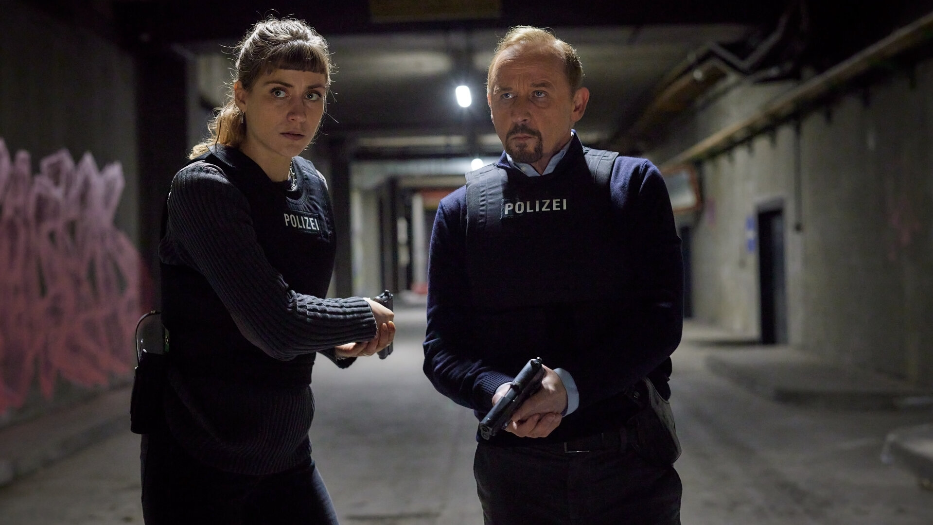 "Stralsund - Der letzte Sieg": Jule Zabek (Sophie Pfennigstorf) und Karl Hidde (Alexander Held) stehen mit gezogenen Waffen und schusssicheren Westen im Tunnelsystem.