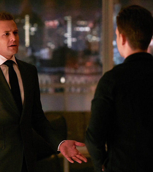 "Suits - Wem die Stunde schlägt": Harvey (Gabriel Macht) und Mike (Patrick J. Adams)  stehen abends im beleuchteten Büro und unterhalten sich. Harvey hält dabei einen Drink in seiner rechten Hand, während er gestikuliert.