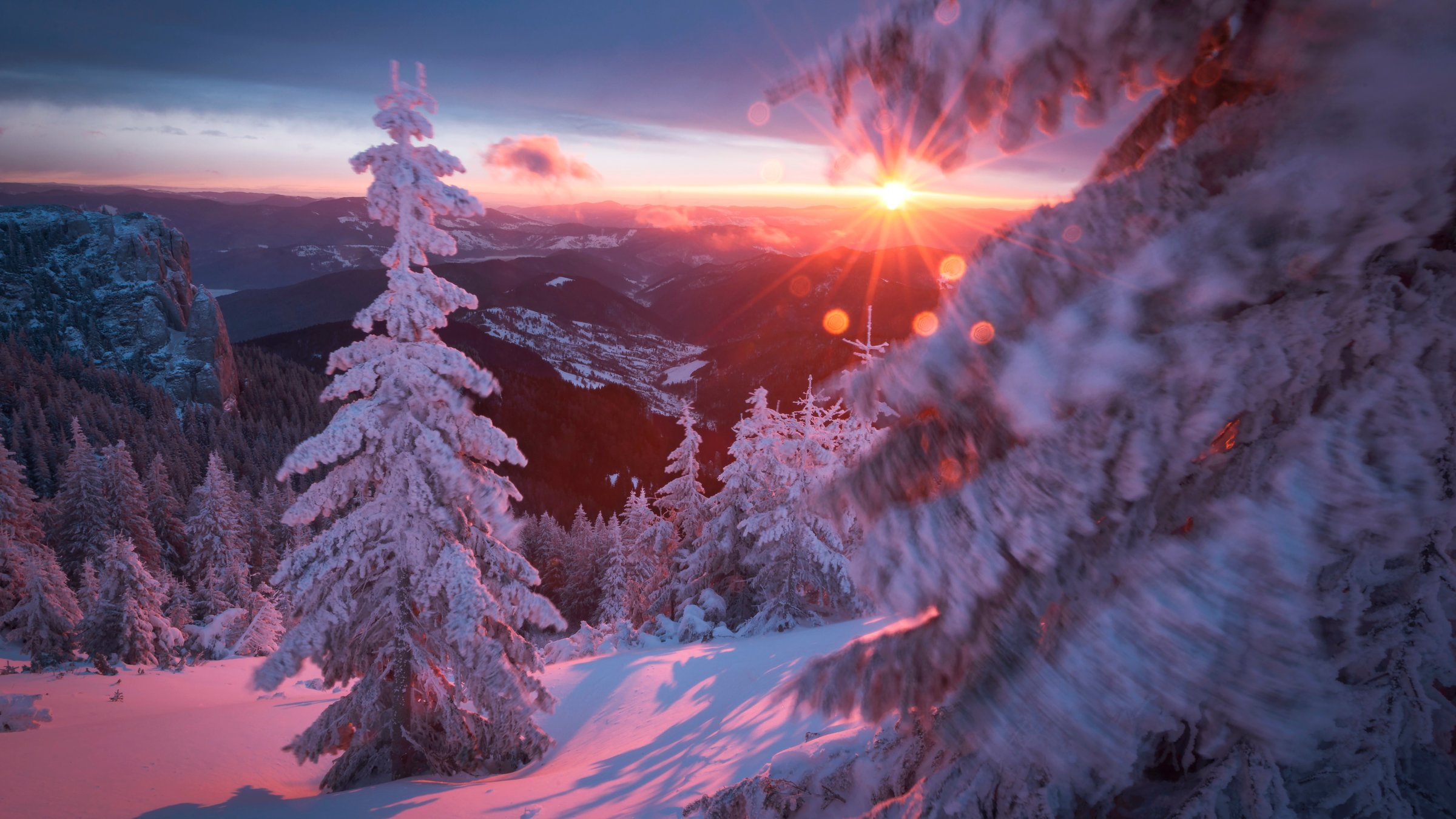 "Rumäniens wilde Schönheit (3/3) - Herbst und Winter": Schneebedeckte Tannen vor untergehender Sonne in einer winterlichen Mittelgebirgslandschaft.