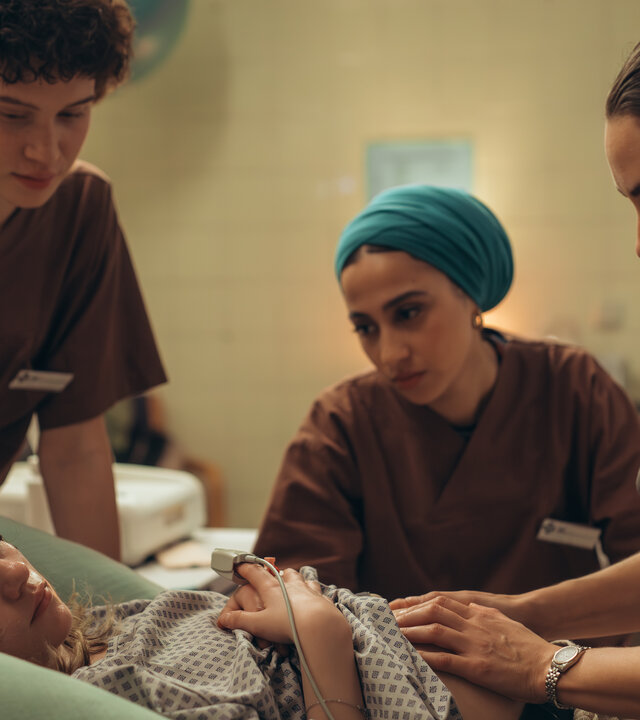 "PUSH - Geheimnisse": Lou (Lisa Moell) liegt in der Klinik. Greta (Lydia Amasko) und Meryem (Tua El-Fawwal) stehen daneben während Dr. Mohn (Katia Fellin) Lou untersucht.