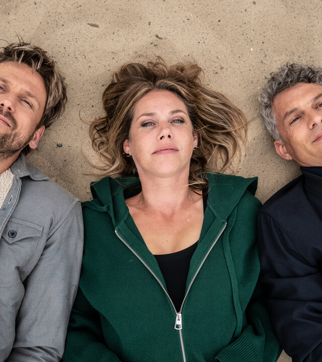 "Neuer Wind im Alten Land - Männer & Gedöns": Blick von oben: Im Sand liegt Beke (Felicitas Woll) Schulter an Schulter zwischen Paul (Steve Windolf) und David (Martin Bretschneider).