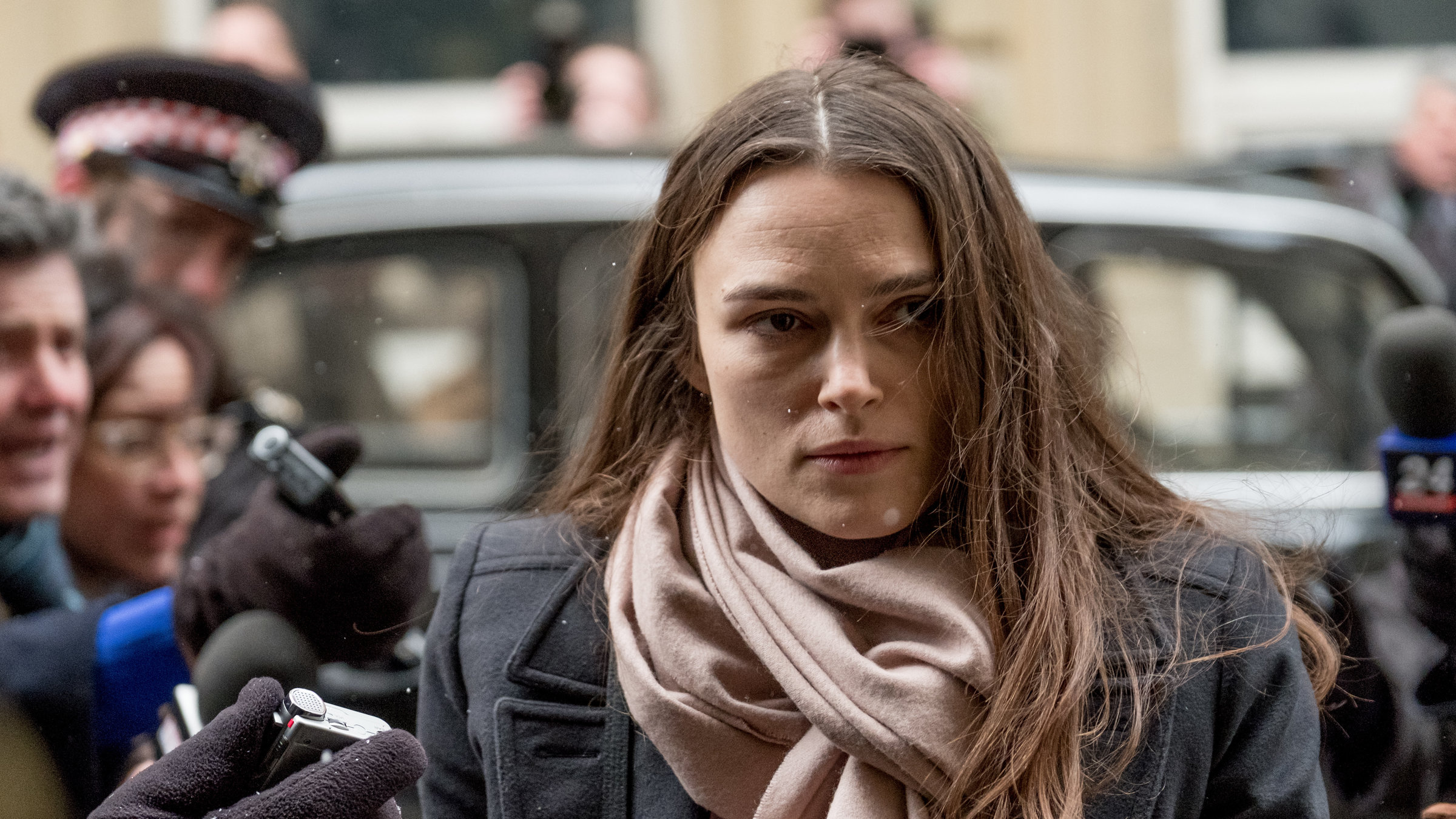 "Official Secrets - Gefährliche Wahrheit": Katharine Gun (Keira Knightley) geht mit gefasstem Blick durch ein Spalier von Reportern, die unscharf links und rechts zu erkennen sind. Sie strecken ihr ihre Mikrofone entgegen. Katharine trägt einen Wintermantel und hat einen großen Schal um den Hals gebunden. Die Hände der Reporter stecken in Handschuhen.