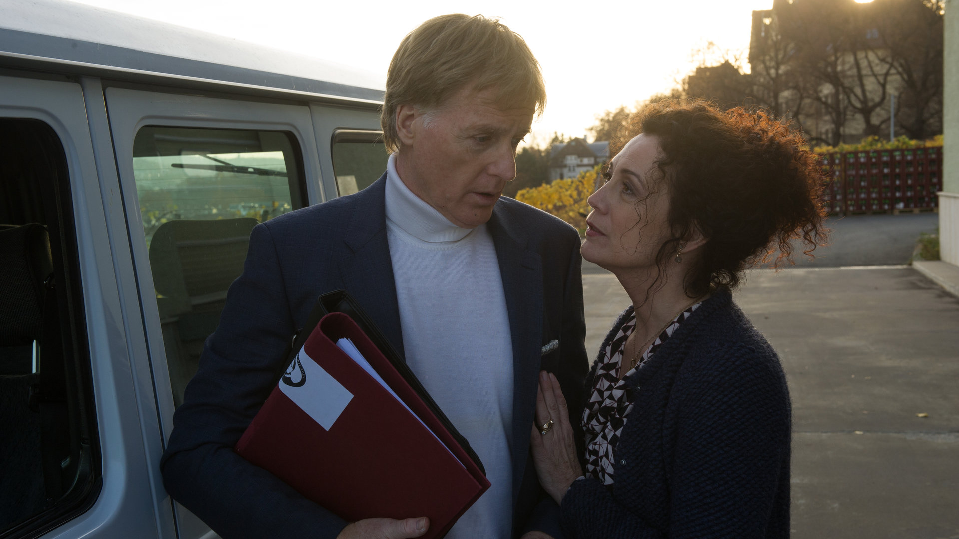 "SOKO Stuttgart - Rendezvous mit dem Tod": Michael (Albert Fortell) und Ariane Ruge (Barbara Wussow) stehen vor einem weißen Lieferwagen auf dem Hof ihres Unternehmens. Im Hintergrund ist durch Bäume eine große alte Villa zu sehen.