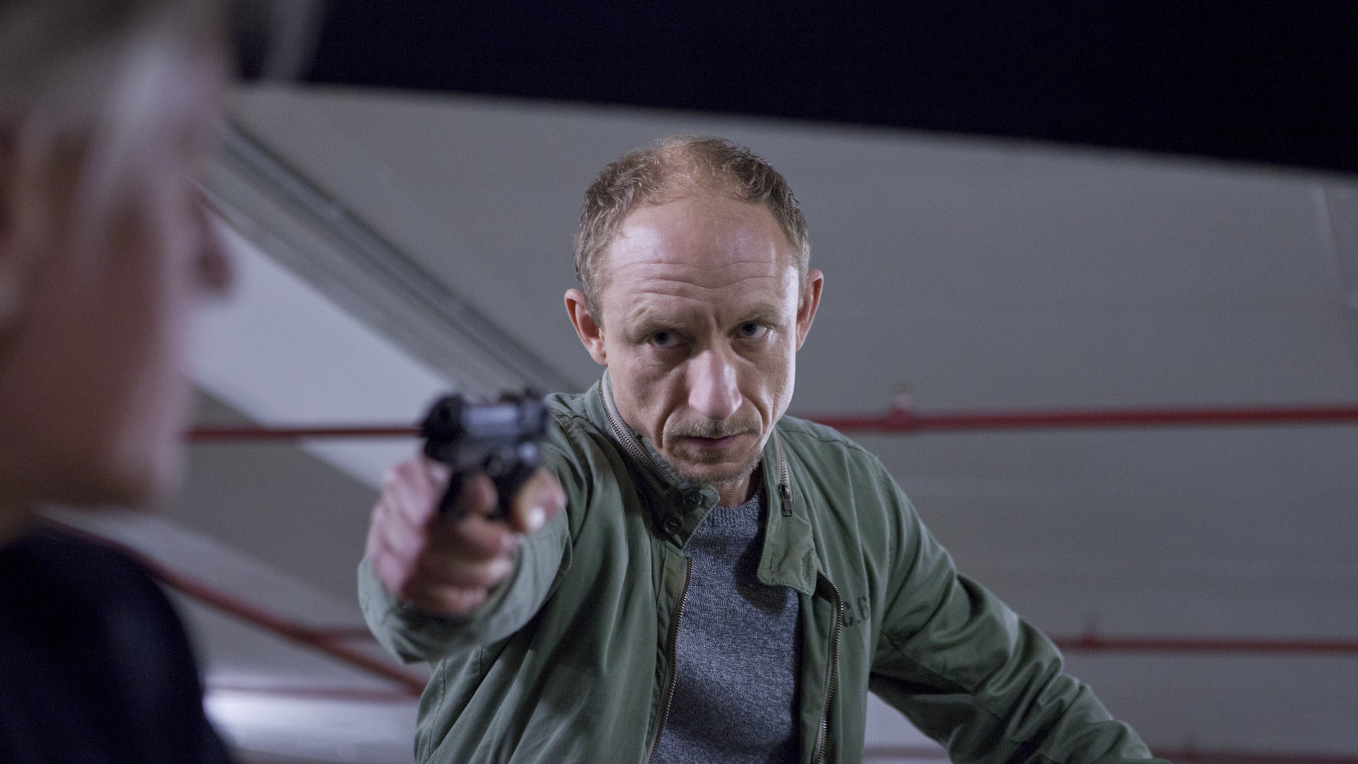 "Wilsberg - Die Entführung": Russ (Michael Schenk) zielt mit der Waffe auf eine Person. Er steht in einer Tiefgarage.