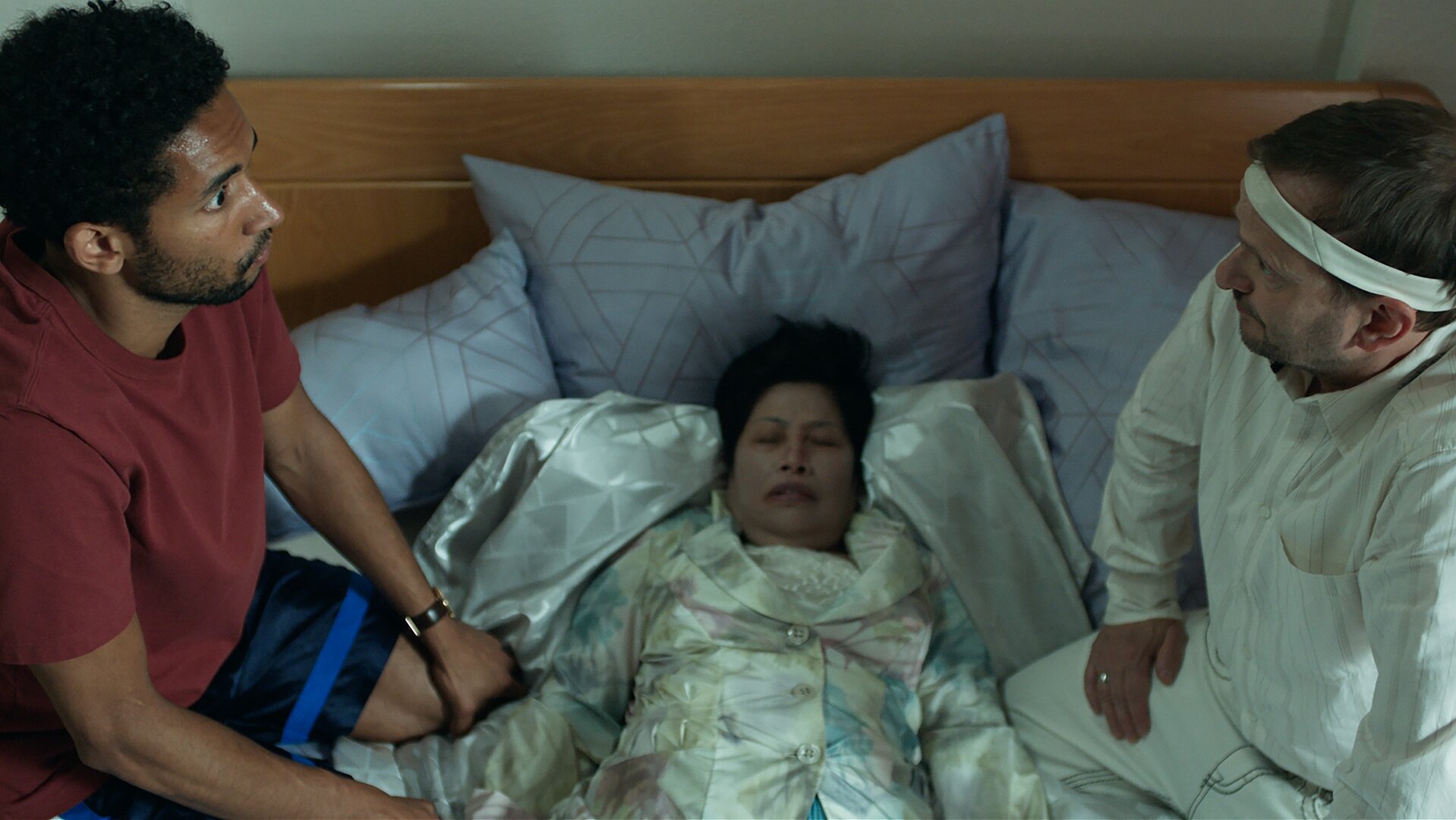"Doppelhaushälfte - Immer Ärger mit Oma Thuy": Theo (Benito Bause) und Andi (Milan Peschel) knien auf dem Bett und schauen sich in die Augen. Zwischen ihnen liegt Oma Thuy.