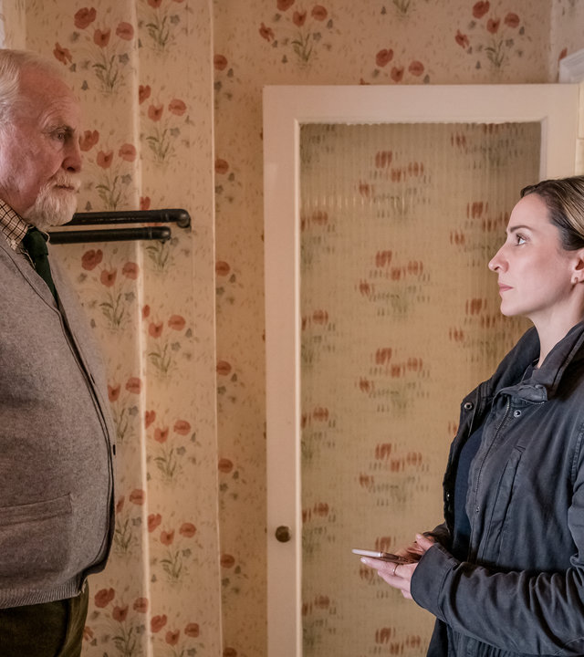 "The Bay - Versäumnis": In einem Wohnzimmer. Lisa Armstrong (Morven Christie) steht vor Bill Bradwell (James Cosmo). Die beiden blicken sich ernst an.