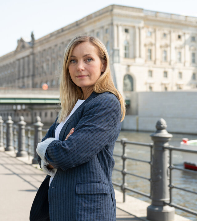 "Die Jägerin - Gegen die Wut": Staatsanwältin Judith Schrader (Nadja Uhl) steht mit verschränkten Armen im Freien vor der Spree. Im Hintergrund steht die Berliner Rathausbrücke.