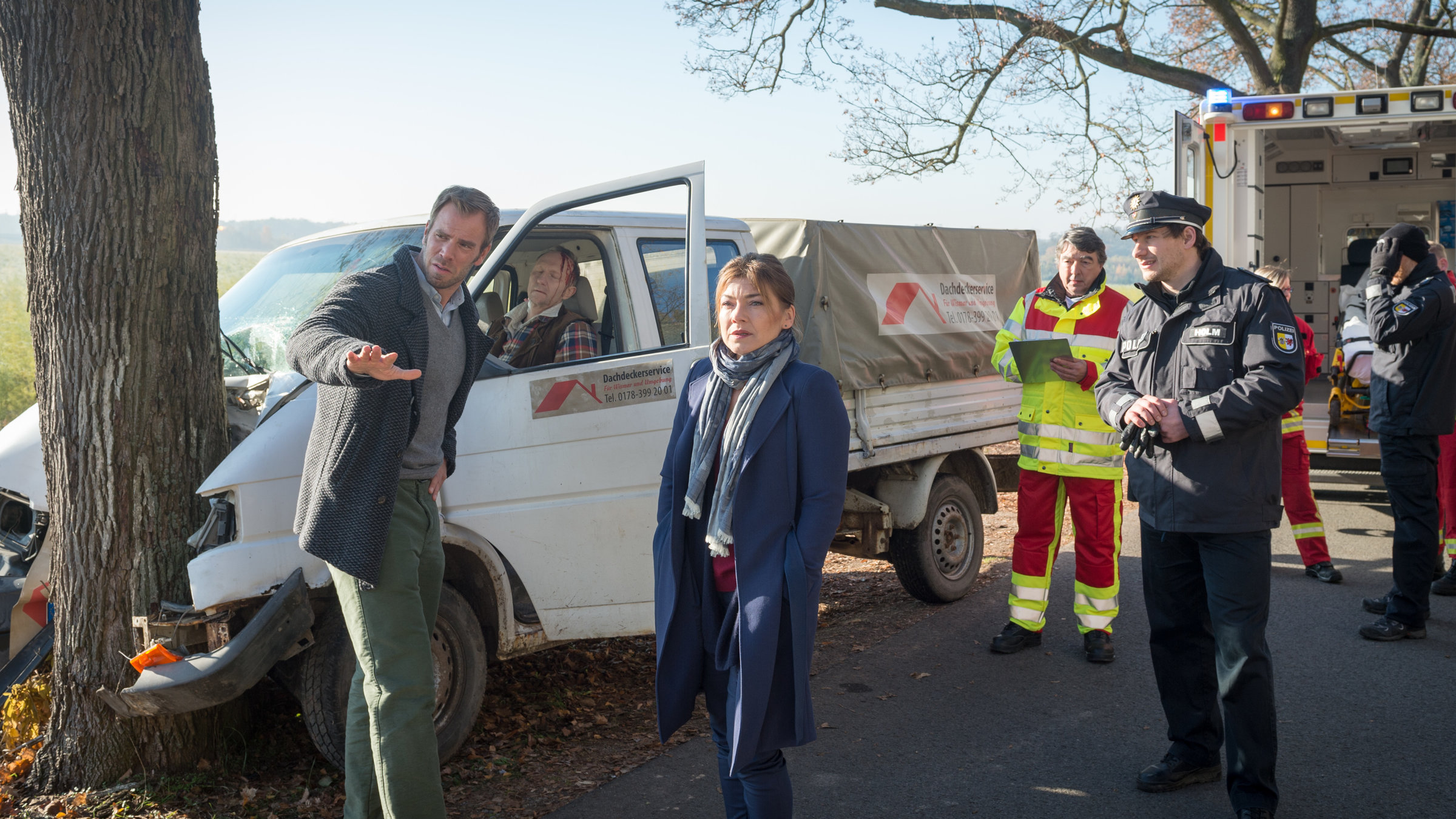 „SOKO Wismar – Der Hai auf dem Dach“: An der Unfallstelle sind Kommissar Lars Pöhlmann (Dominic Boeer), Katrin Börensen (Claudia Schmutzler), Polizist Jens Holm (Felix Defèr) sowie Notarzt Olli (Bernhard Leute) und weitere Rettungssanitäter. Der Unfallwagen, in dem das Opfer Werner Kleinschmidt (Alexander Hauff) sitzt, sind im Hintergrund zu sehen.