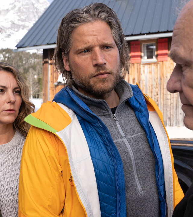 "Die Bergretter: Roter Schnee (2)": Auf dem schneebedeckten Hof steht Markus (Sebastian Ströbel) mit ernster Miene zwischen Katharina (Luise Bähr) und ihrem Vater Peter Herbrechter (Michael König).