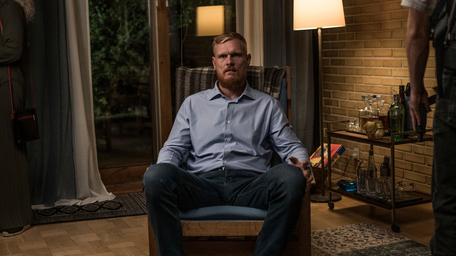 "Elvira - Da rein da raus": Kommissar Køster (Peter Plaugborg) sitzt breitbeinig auf einem Designersessel in seinem Wohnzimmer und starrt ins Leere.