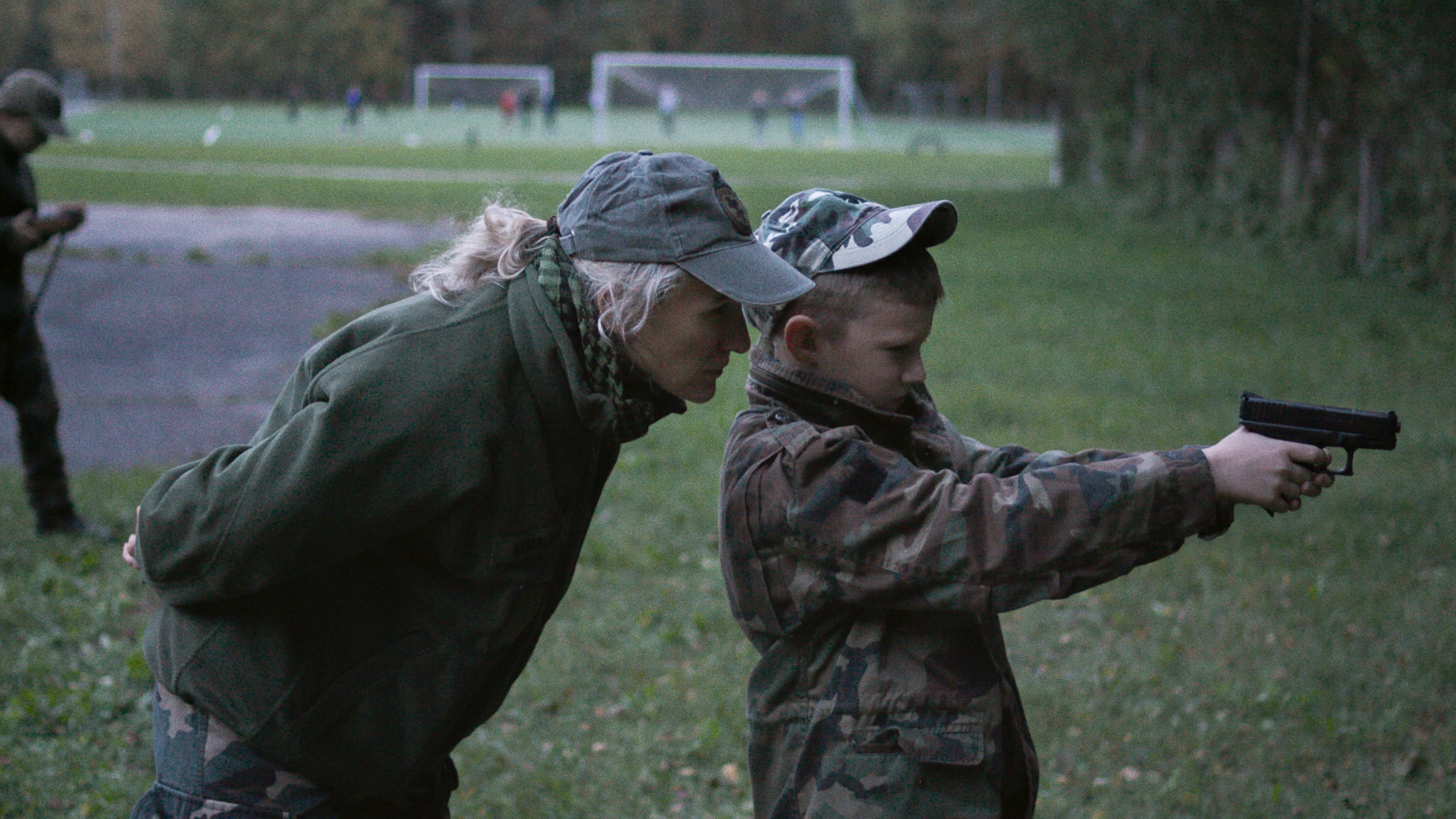 "RUKLA - Momentan keine Feindsicht": Vilma Akvilė Karoblienė steht hinter ihrem Sohn und blickt ihm über die Schulter, während er den Umgang mit einer Pistole trainiert.