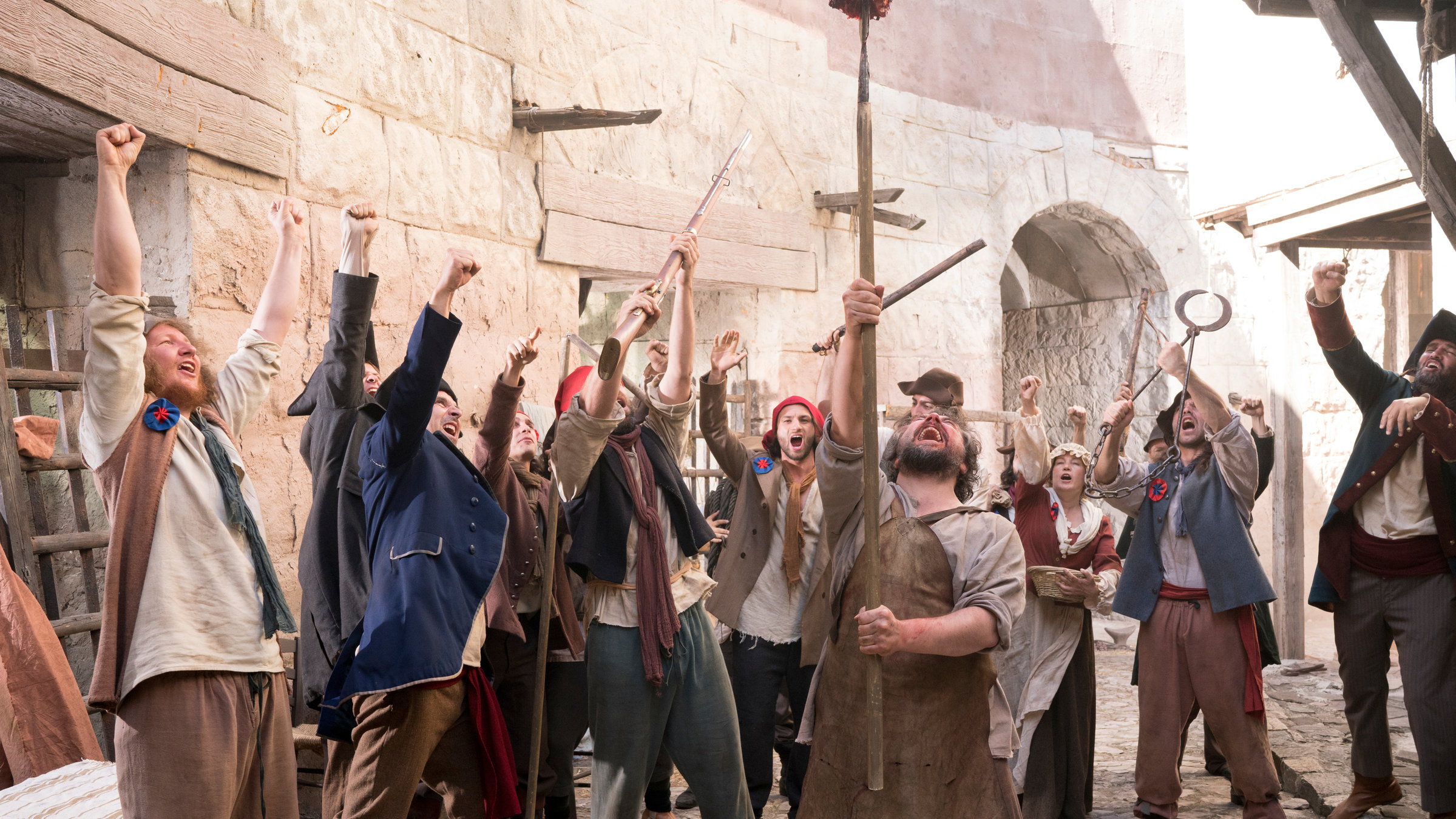 "Terra X: Ein Moment in der Geschichte: Der Sturm auf die Bastille": Spielszene: Im Hintergrund steinerne Hausgänge, davor eine Gruppe von Darstellern in Alltagskleidung des 18. Jahrhunderts. Sie recken jubelnd die Hände in die Höhe.