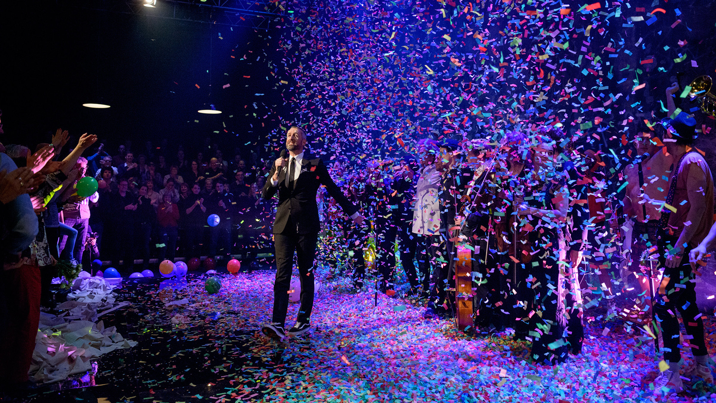 "Pufpaffs Happy Hour - Jubiläumssendung 50. Folge": Sebastian Pufpaff steht auf der Bühne. Er trägt, wie immer, einen schwarzen Anzug mit weißem Hemd und einer schwarzen Krawatte, dazu Turnschuhe. Auf der Bühne regnet es Konfetti. Viele bunte Luftballons liegen bereits auf der Bühne. Hinter ihm stehen alle Gäste dieser 50. Jubiläumssendung. Die Zuschauer stehen und applaudieren ihrem Gastgeber.
