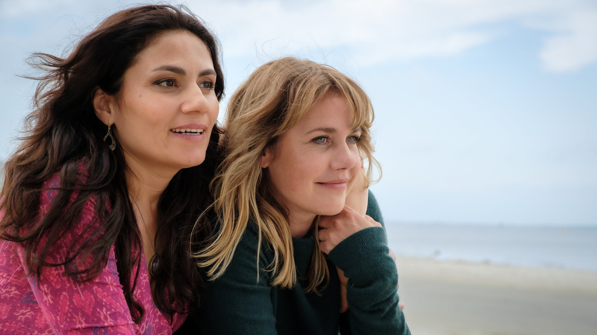 "Neuer Wind im Alten Land – Gestrandet": Beke (Felicitas Woll) und Elif (Halima Ilter) sitzen nebeneinander am Strand und blicken aufs Wasser.
