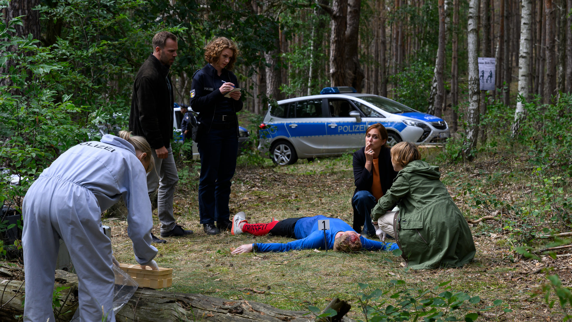 „SOKO Wismar – Der Berg ruft“: Dr. Helene Sturbeck (Katharina Blaschke), Paula Moorkamp (Stella Hinrichs), Lars Pöhlmann (Dominic Boeer) und Karoline Joost (Nike Fuhrmann) haben sich um den toten Toni Leitner (Christoph von Friedl) im Wald versammelt. Roswitha Prinzler (Silke Matthias) sucht nach Spuren.